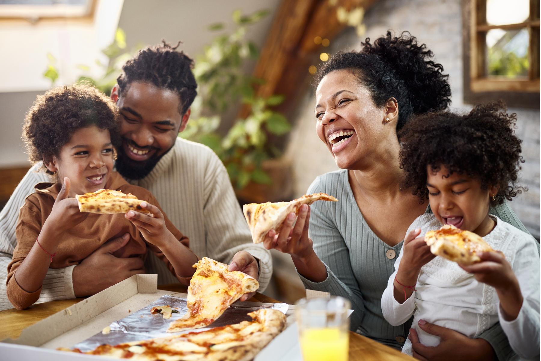 Mother, father, son, and daugher laughing and eating cheese pizza together