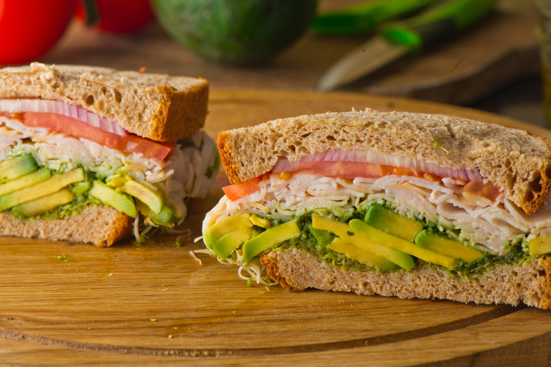 turkey and avocado sandwich with sliced tomato, red onion, and sprouts on whole grain bread