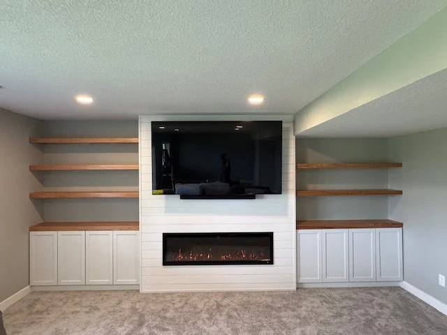 Living room with built-in white cabinets, floating wooden shelves, a flat-screen TV, and a modern electric fireplace.