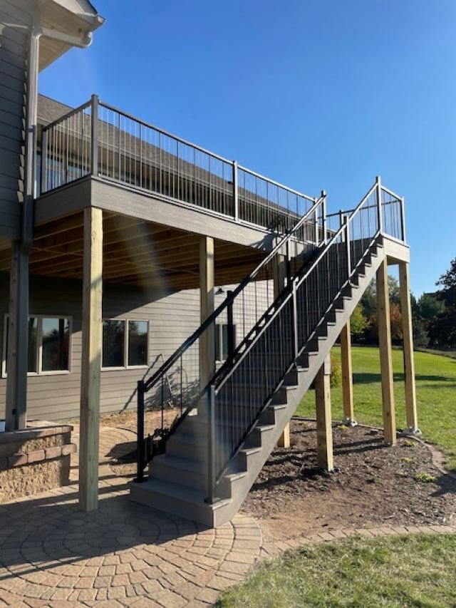 Outside view of a house with new composite deck and metal staircase leading up to the deck, sunny day, green lawn.