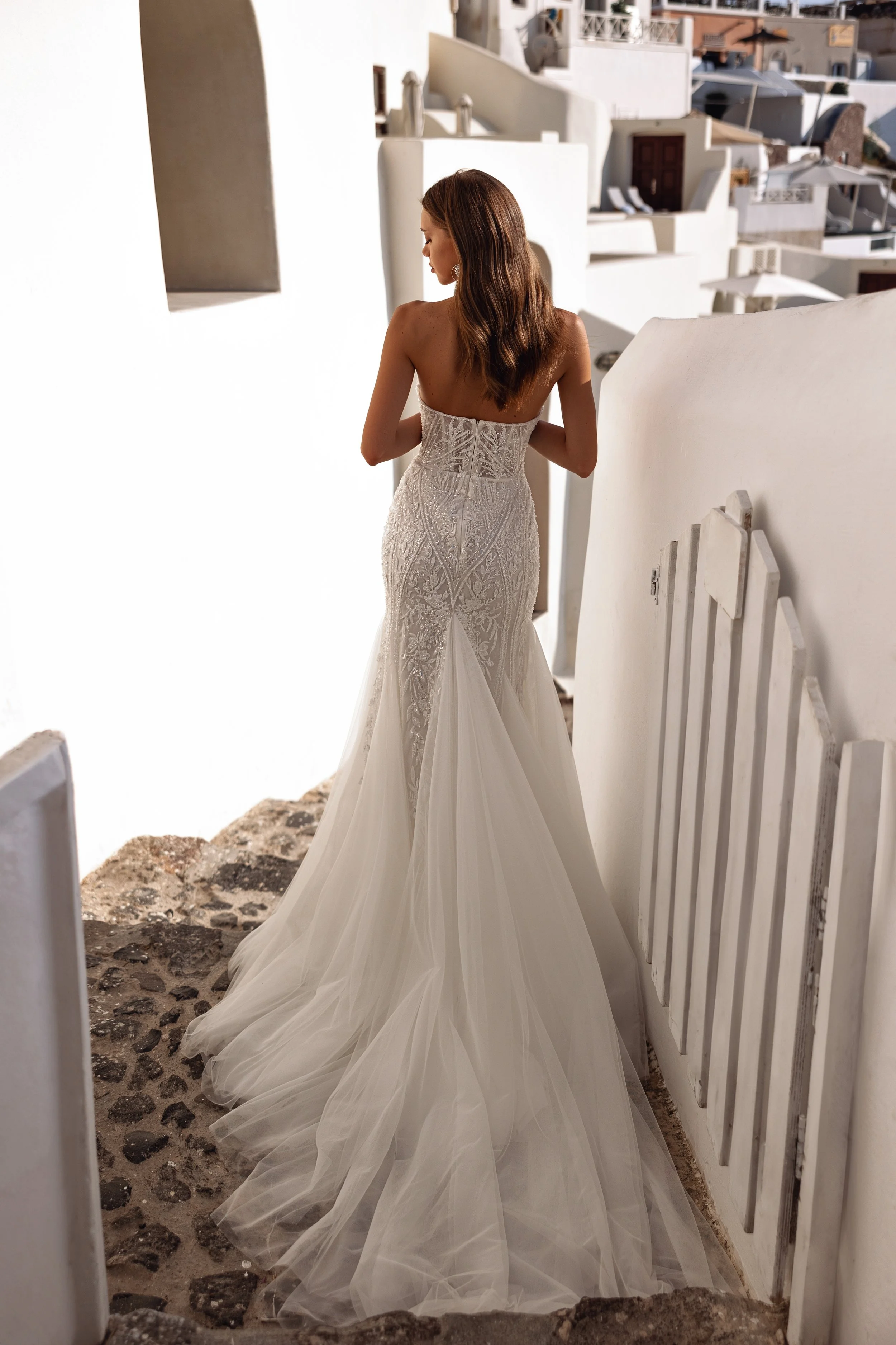 Back view of a beaded mermaid bridal gown featuring crystal button details and a flowing tulle shawl.