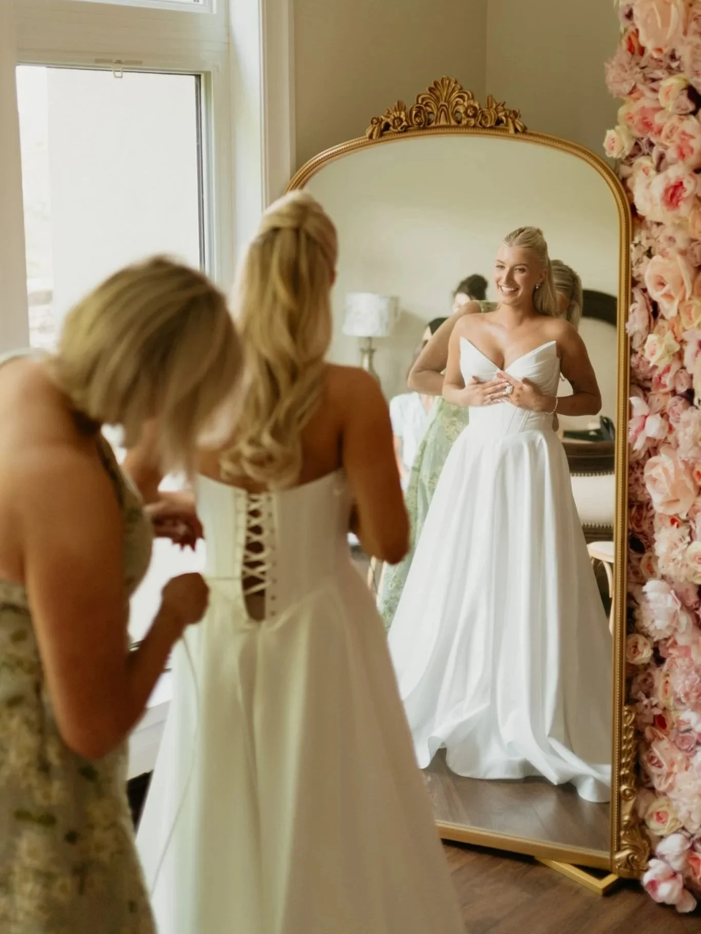 Mother of the bride is helping her daugher put on a wedding dress with a corset