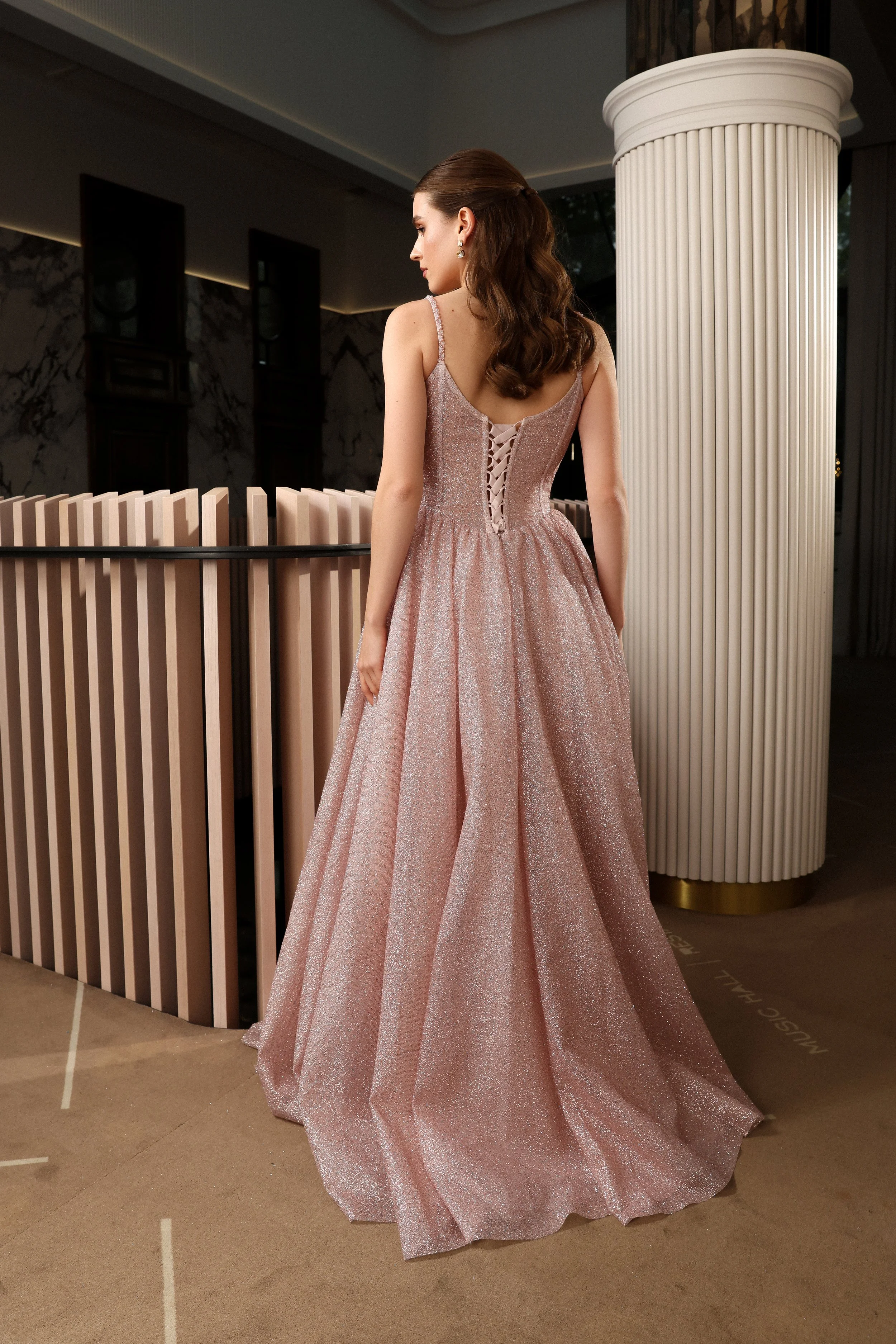 Back view of a baby pink glitter evening gown featuring a corset back, beaded straps, and shimmering fabric.