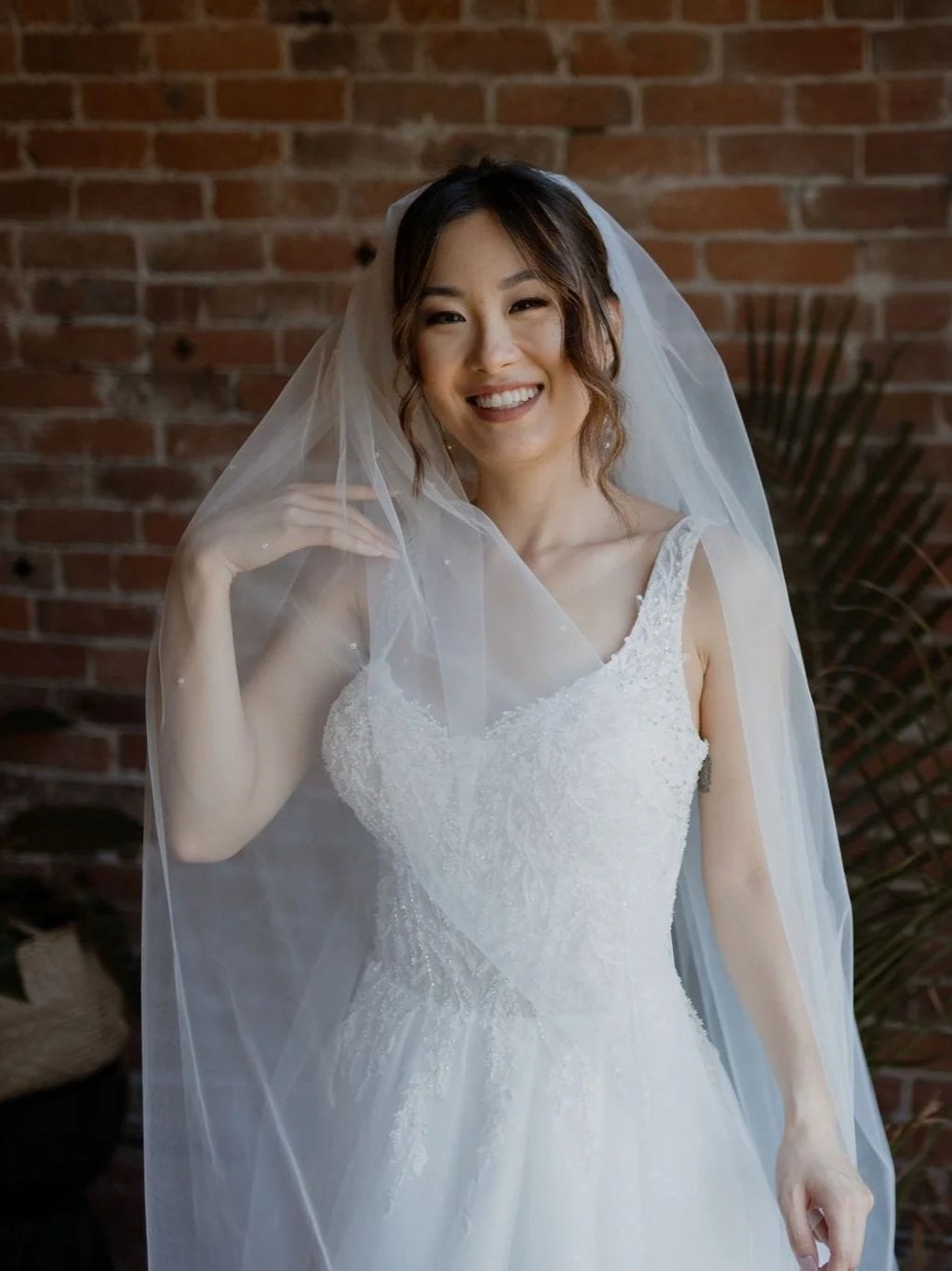 Bride close up in a wedding gown holding up her veil.