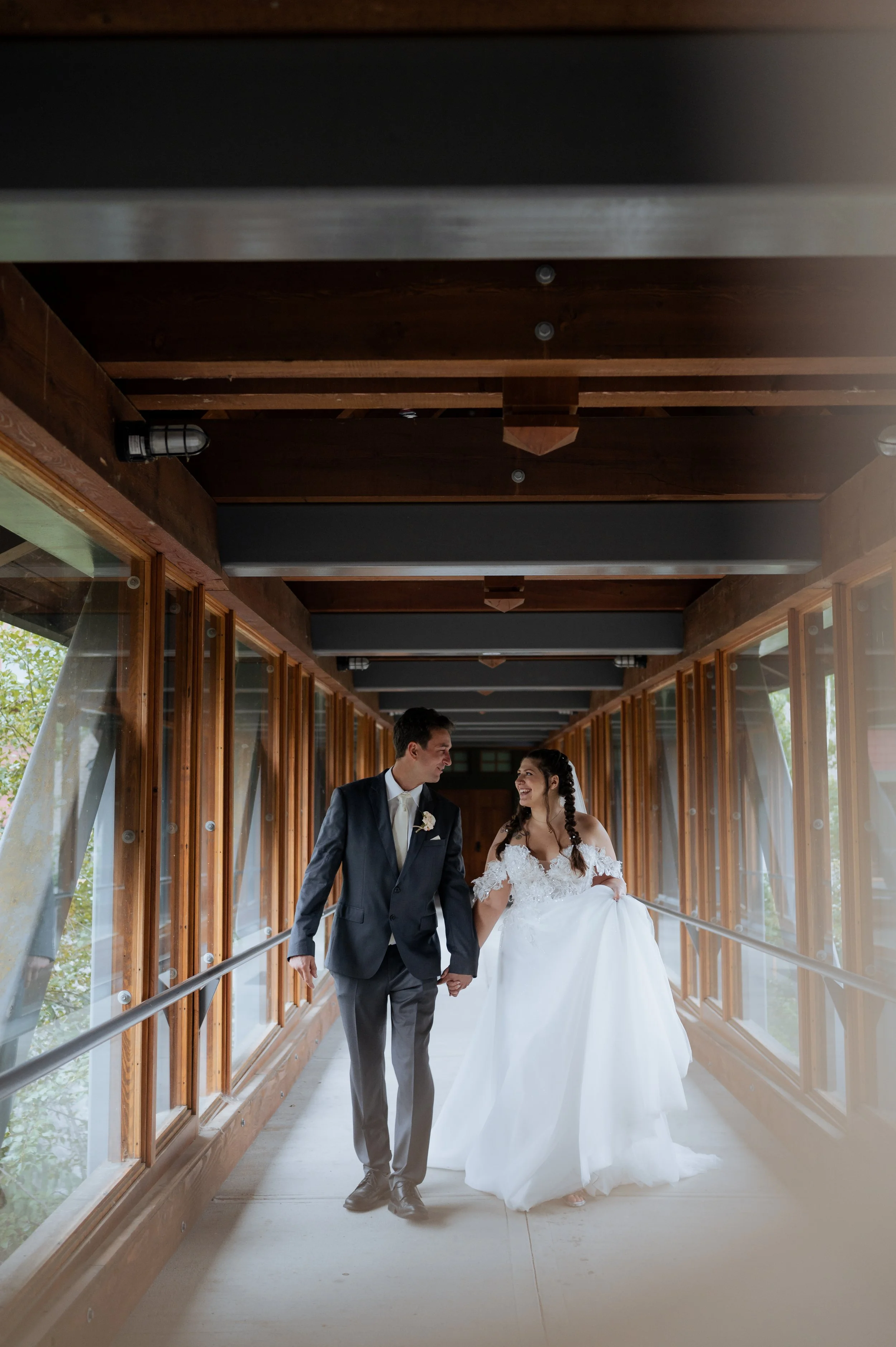 A bride and groom walking hand in hand through a wooden enclosed walkway, smiling at each other during their wedding.