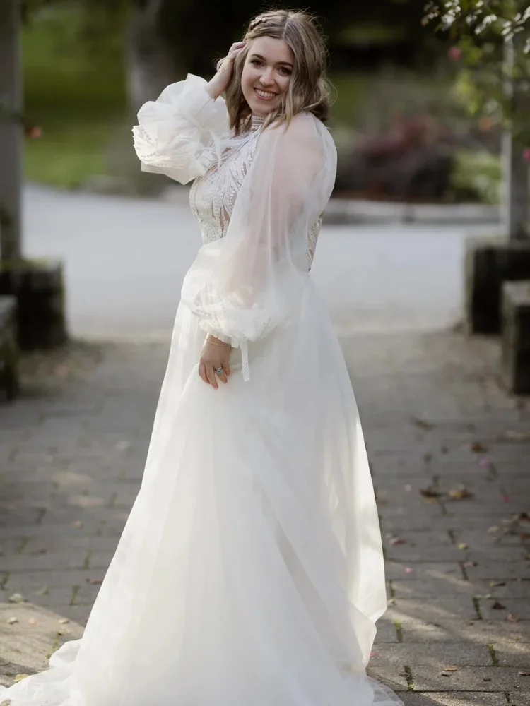 Bride in the Shana vintage-style gown by Tatiana Kaplun with sheer puff sleeves and a high lace neckline, in a garden