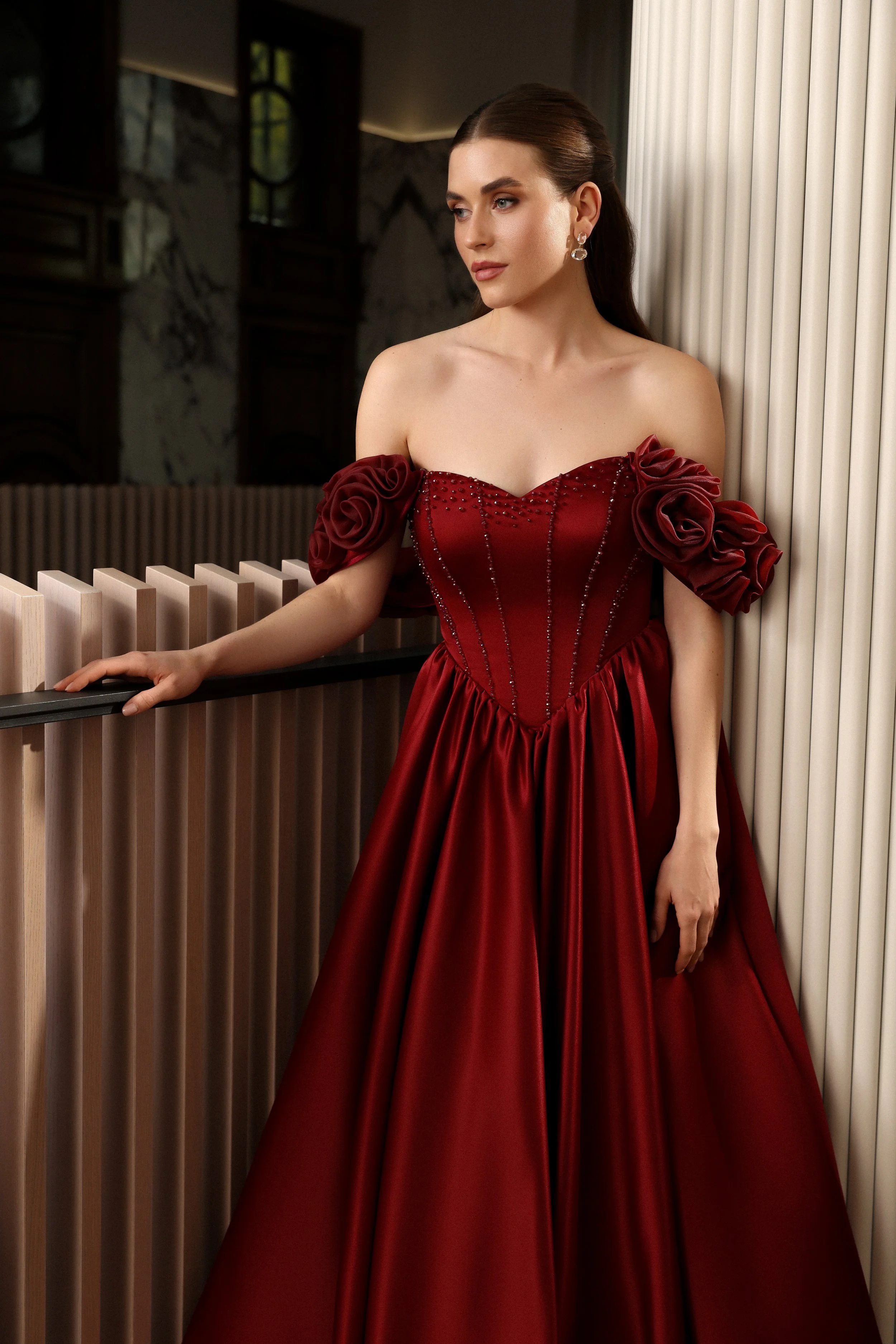 Close view of a designer wine red evening gown with rose floral off the shoulder straps and a fitted silhouette.