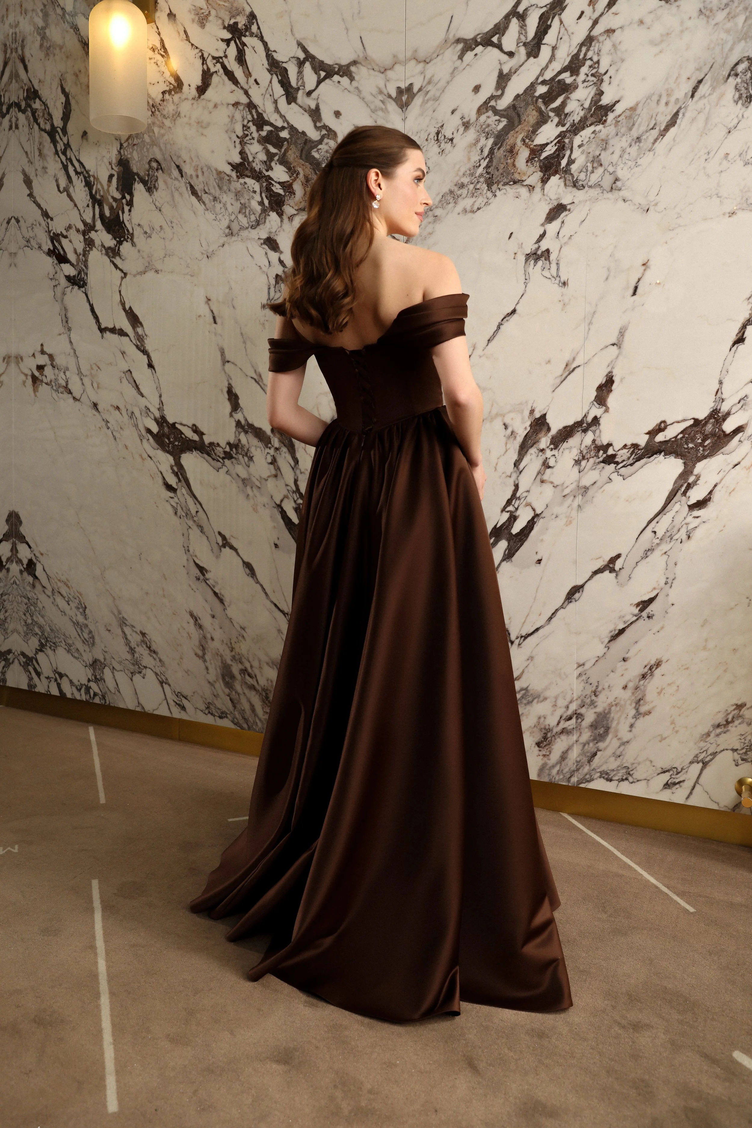 Back view of a designer brown satin evening gown with a fitted silhouette, basque waist, and elegant beaded details.