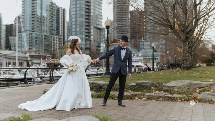Bride in a ballgown wedding dress with boquet, holding hands with groom walking through the city.