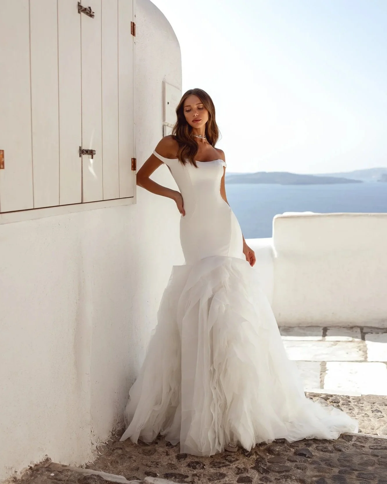 Model wearing a dramatic crepe fitted trumpet wedding gown with statement tulle and organza ruffles.