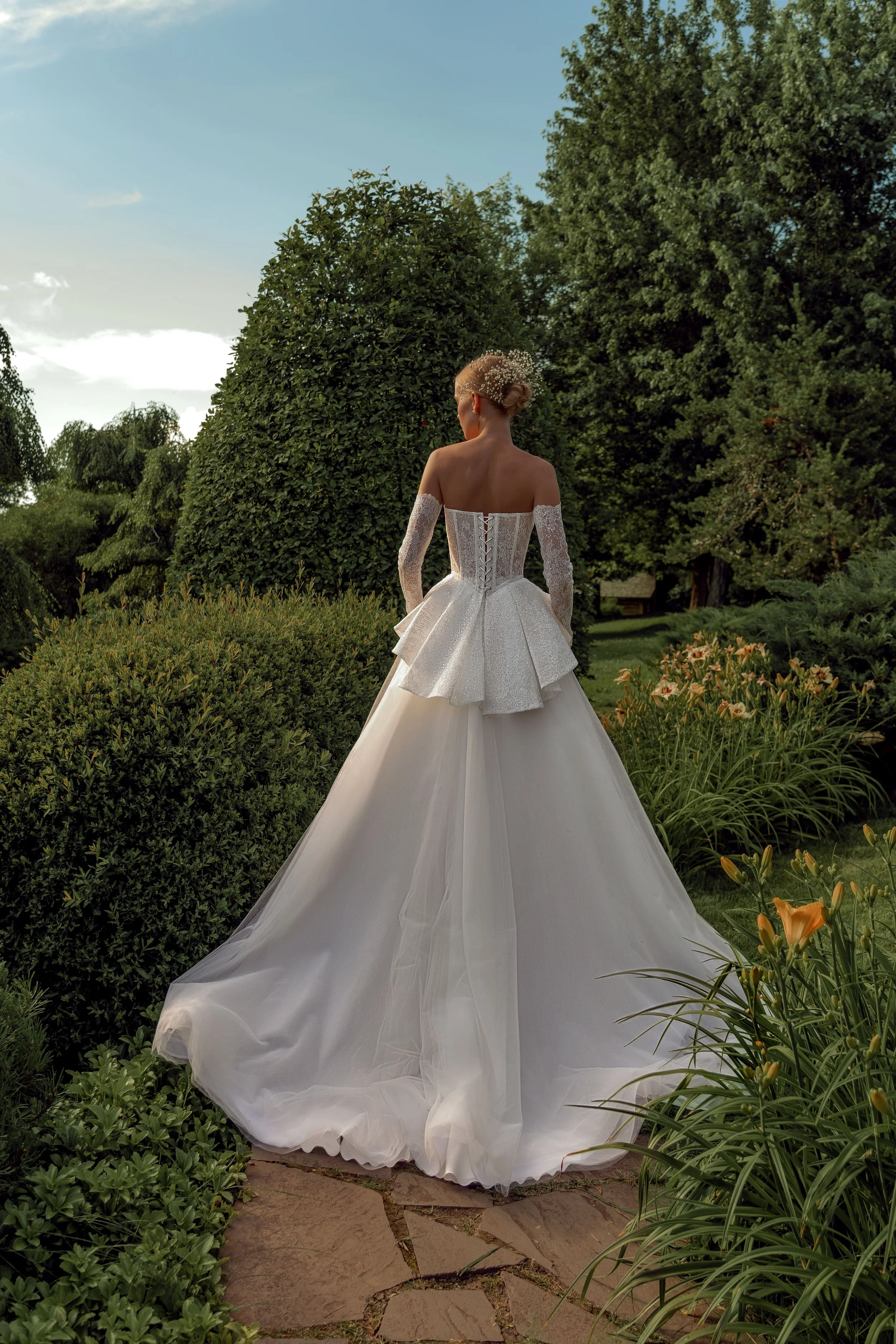 ack view of the Kaimana wedding dress showing the lace and sequin corset, peplum, glittering lace sleeves, and tulle skirt.
