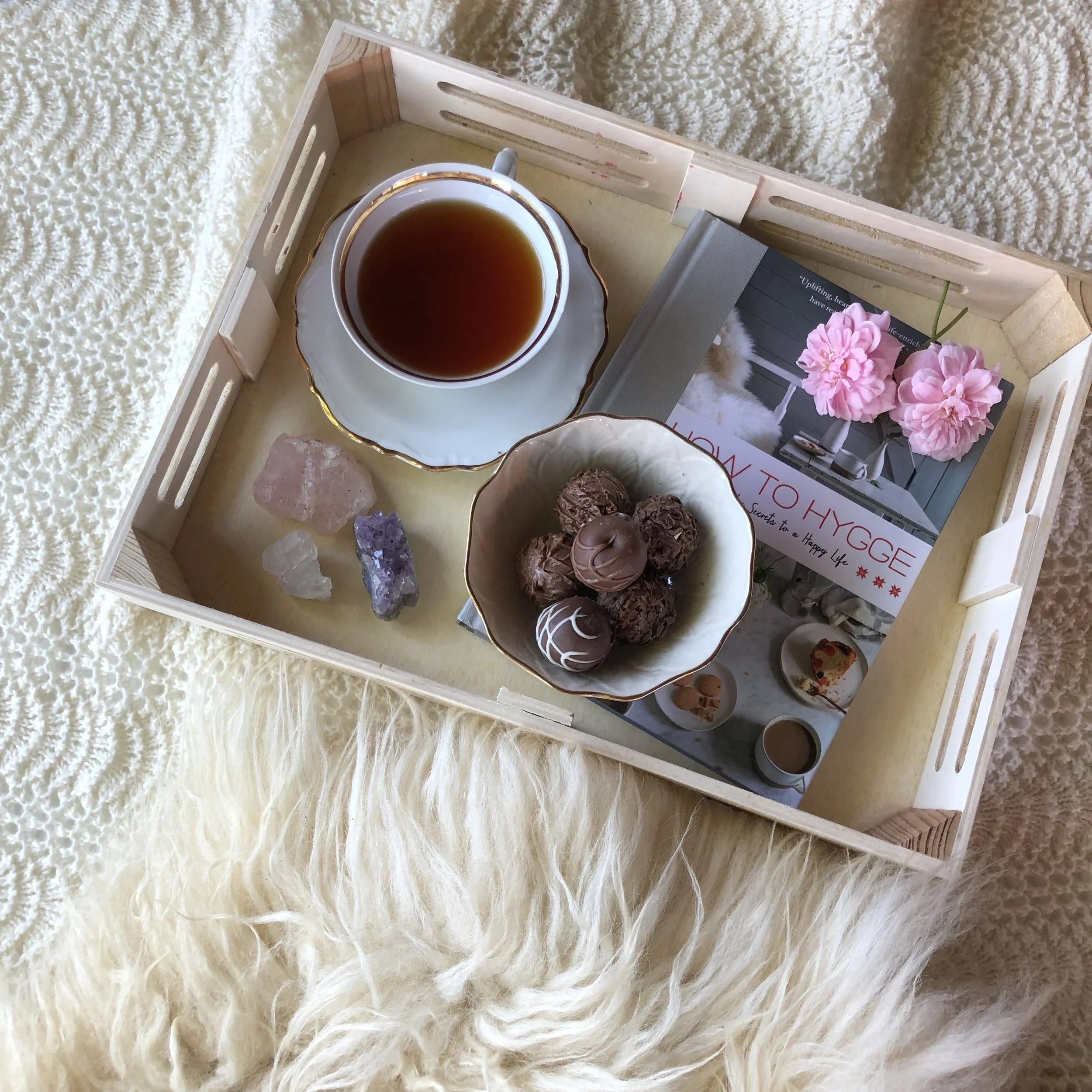 Cozy picture of cup of tea, chocolates, hygge book and crystals on a tray