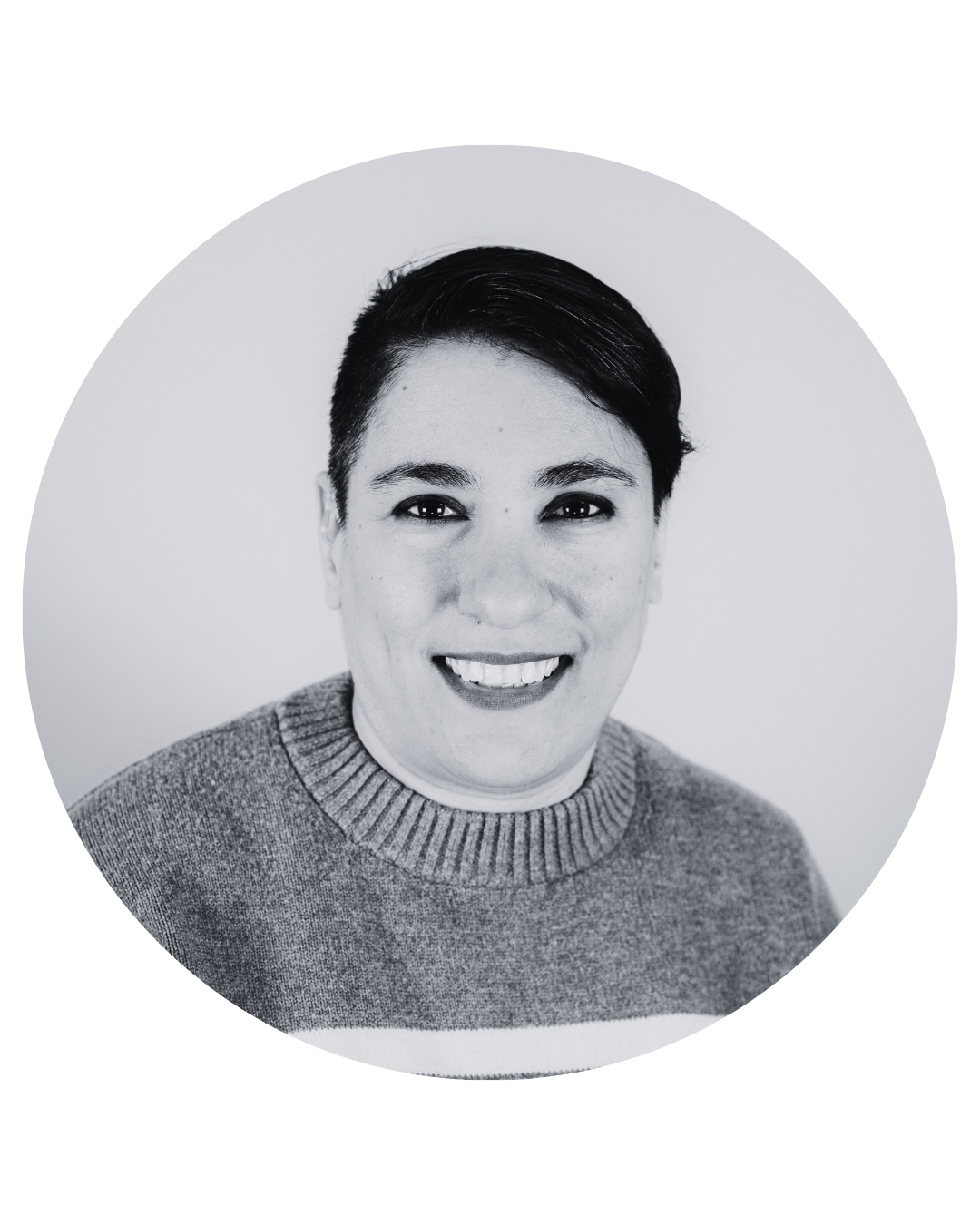 Black and white photo. Ladan is a young woman with medium-length combed-over hair. She wears a striped sweater and smiles widely.