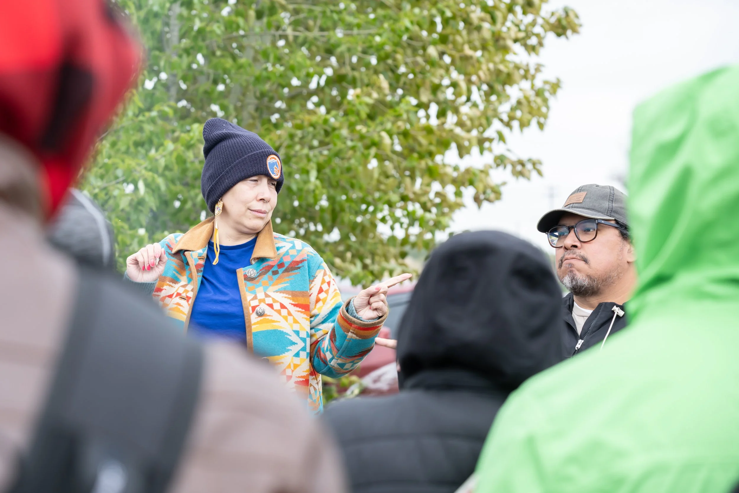 Crystal, an Indigenous woman, addresses a crowd while Torrie looks on.