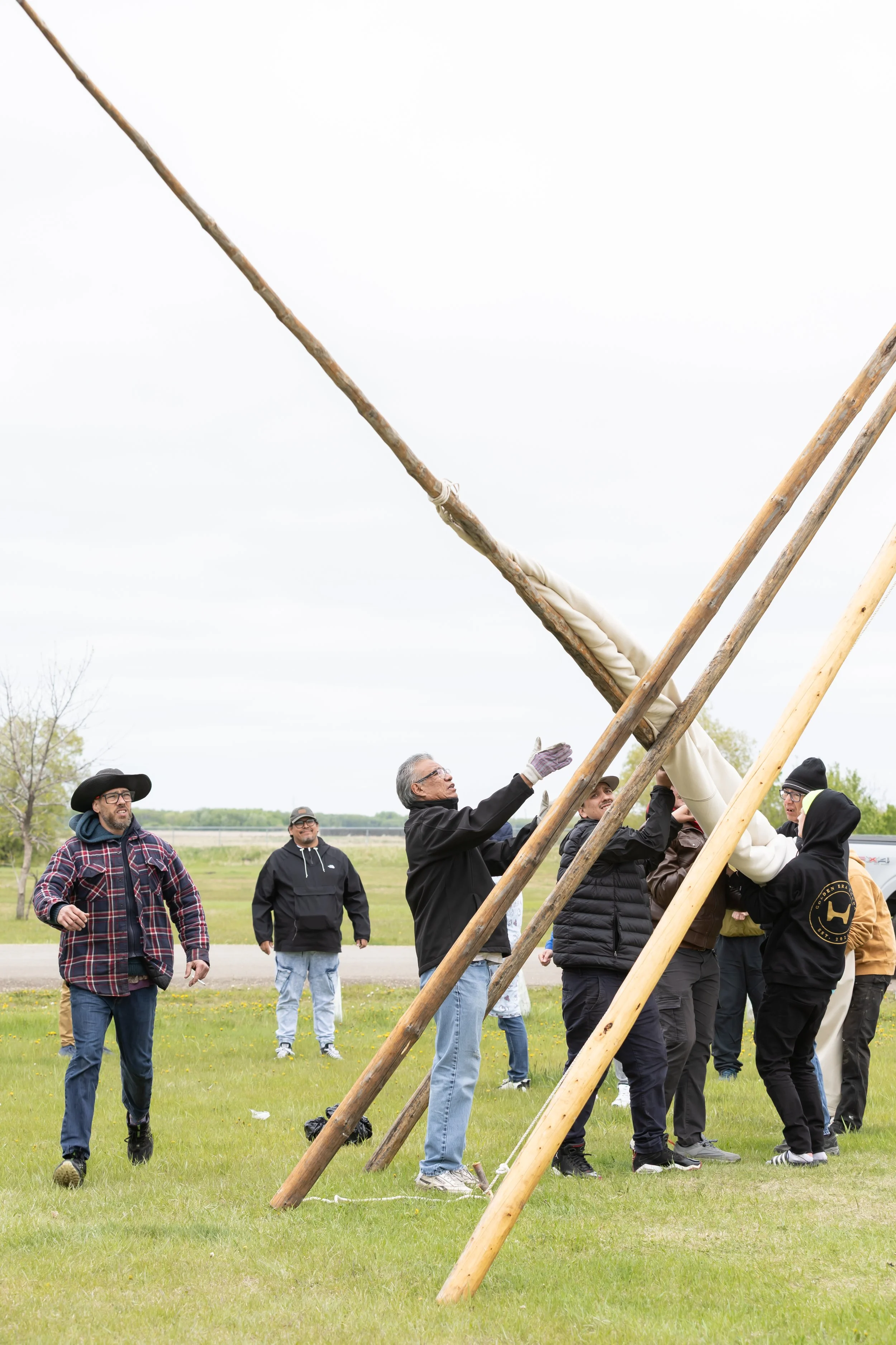 A few people handle a long thin log as part of the teepee lowering ceremony.