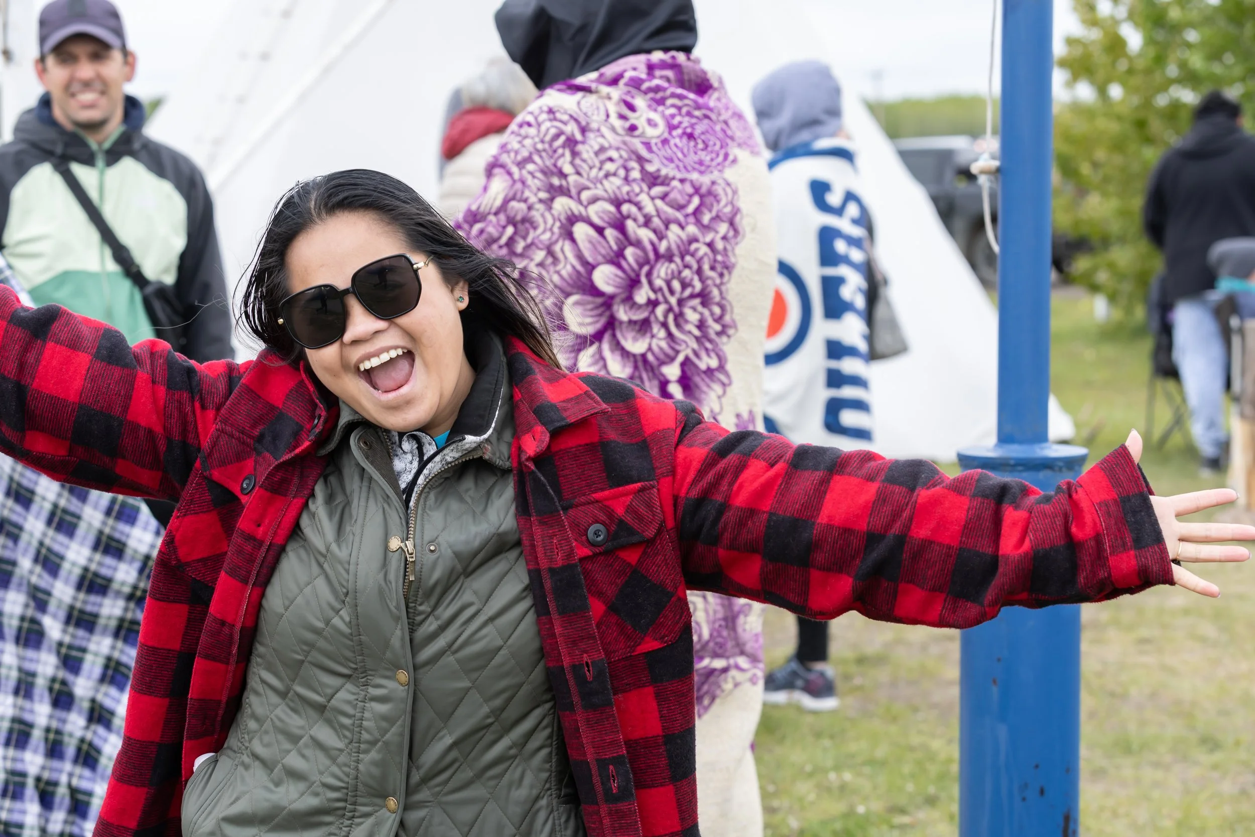 A young woman wearing a red plaid jacket grins widely and poses for the camera.