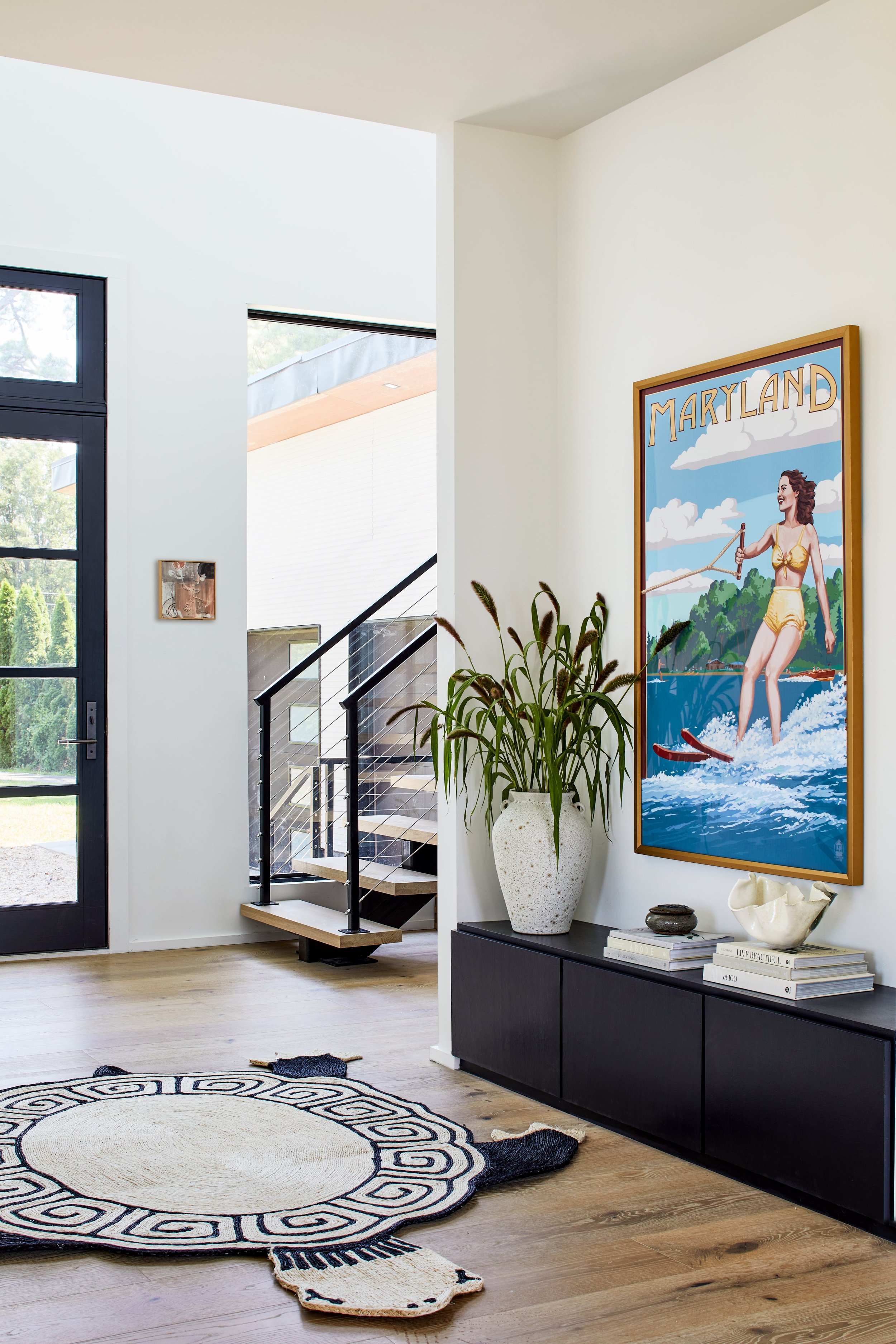 Modern interior with a black front door, a staircase with black railings, a large potted plant, and a colorful Maryland poster on the wall.