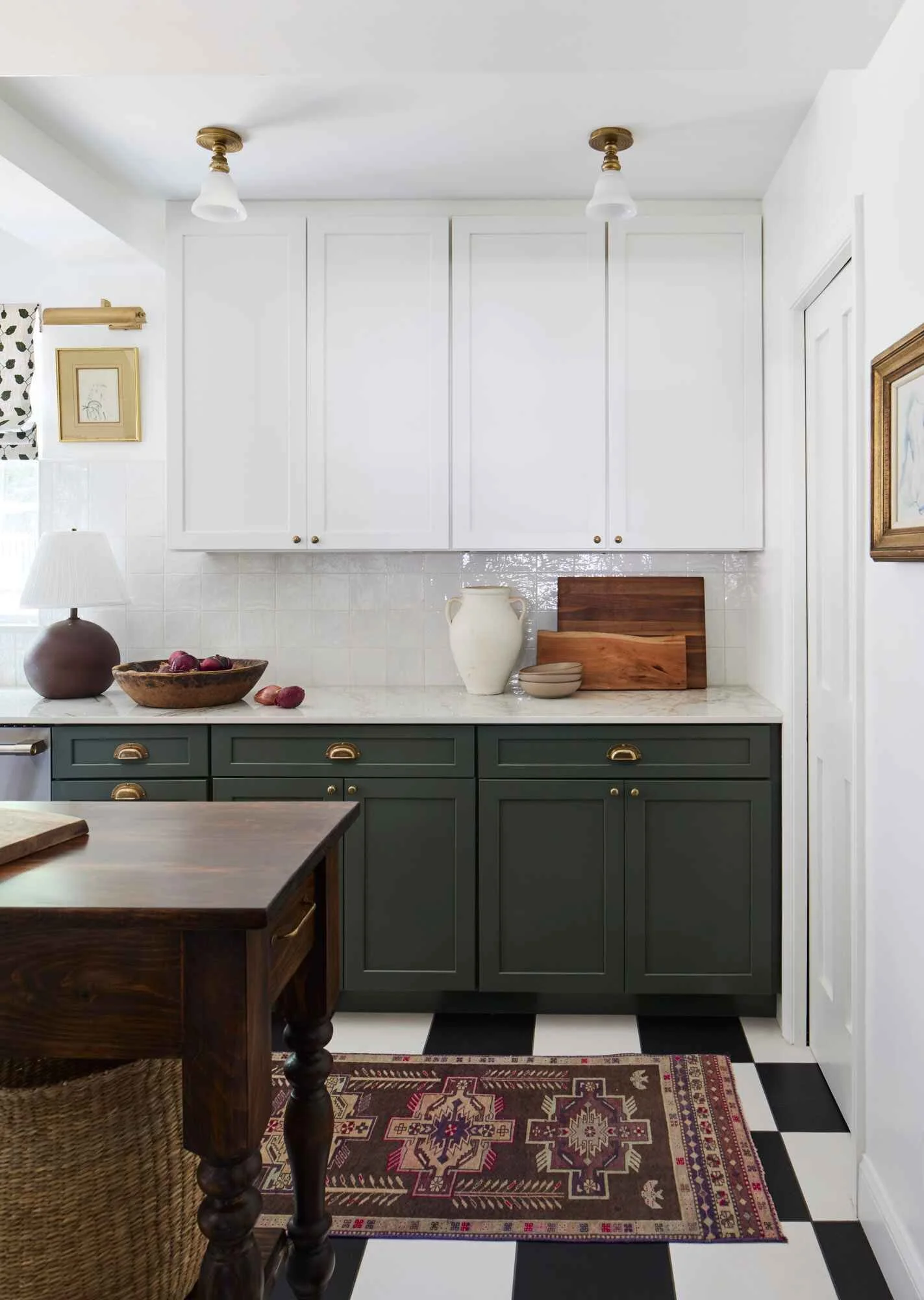 Kitchen with white upper cabinets, dark green lower cabinets, black and white checkered floor, decorative area rug, and countertop with decorative items.