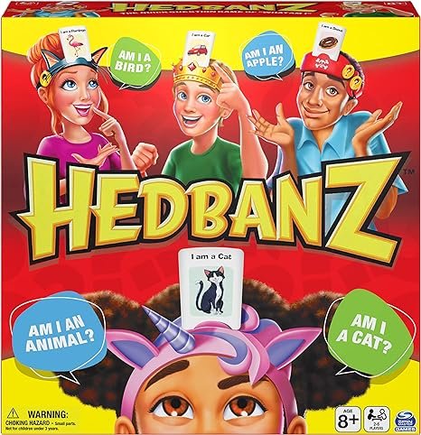 Hedbanz game box featuring three children, one dressed as a cat and others as a unicorn and a scientist, with questions like "Am I a bird?", "Am I an apple?", "Am I an animal?", and "Am I a cat?".