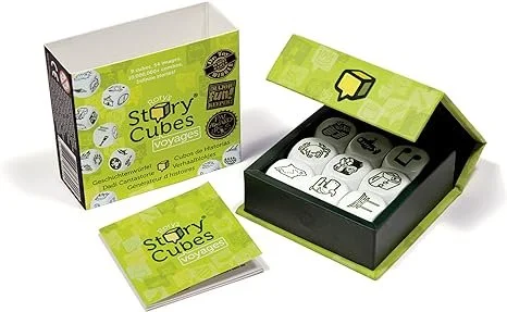 A green and black box of Story Cubes Voyage game, with the lid open showing game pieces inside and an instruction booklet next to the box.