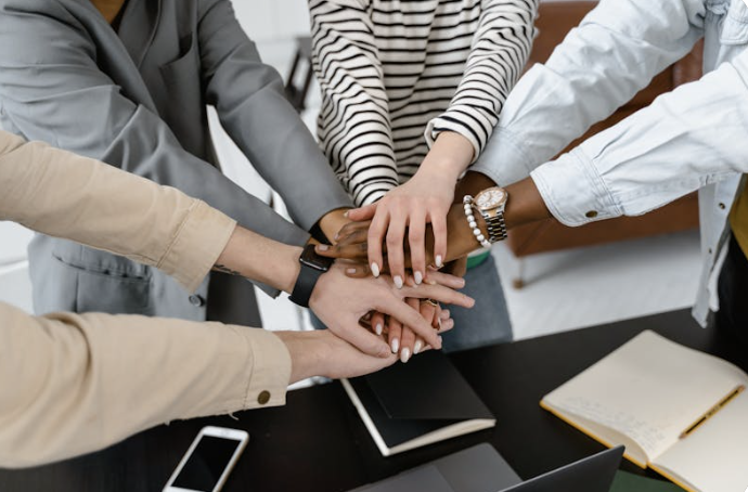 People joining hands in a team gesture around a conference table.