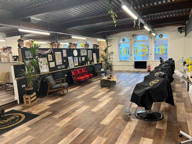Interior of a hair or barber salon with salon chairs, large windows, wall decor, plants, and equipment for hairdressing.