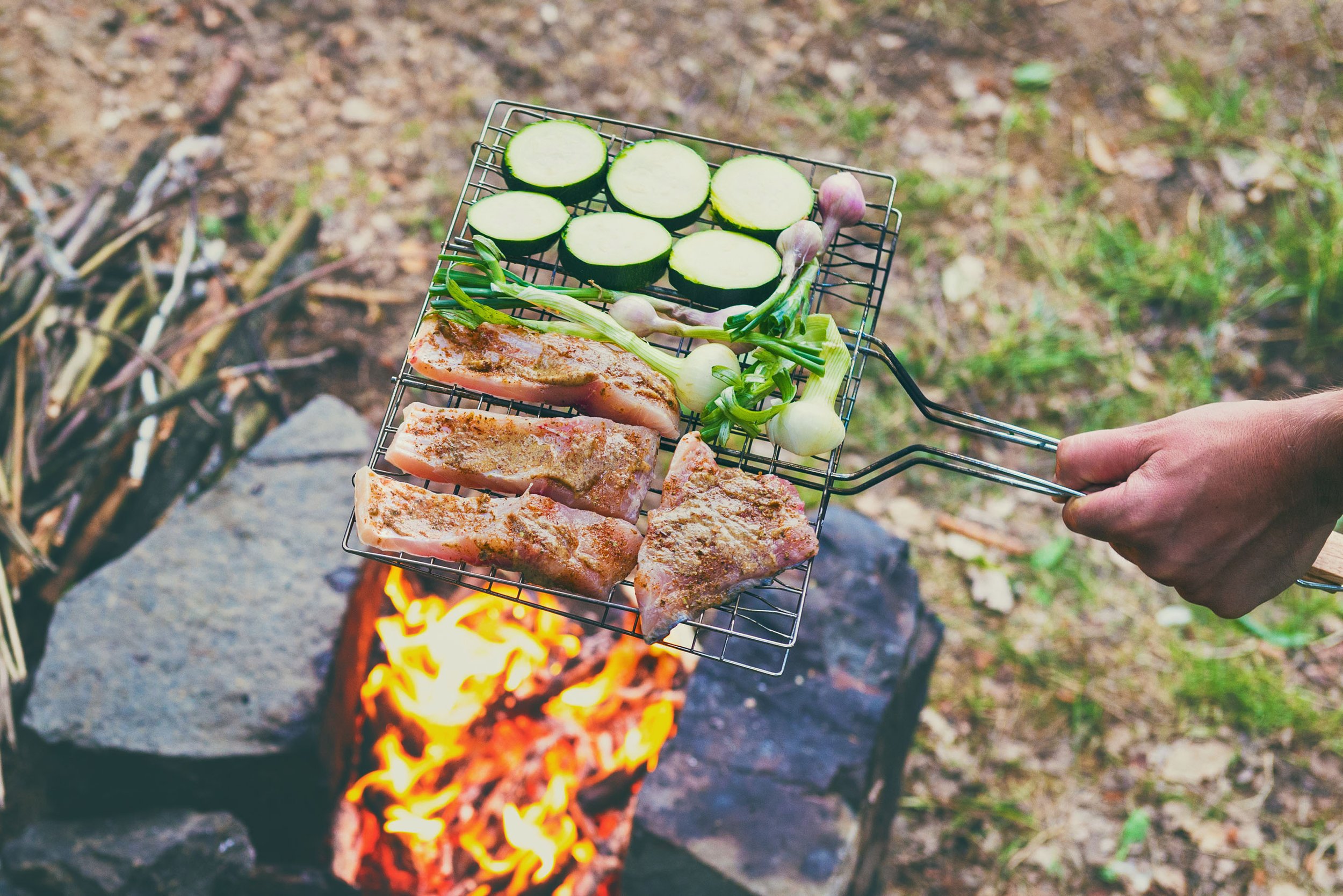 Barbecue extérieur avec des légumes coupés et de la viande sur une grille au-dessus d'un feu de bois.
