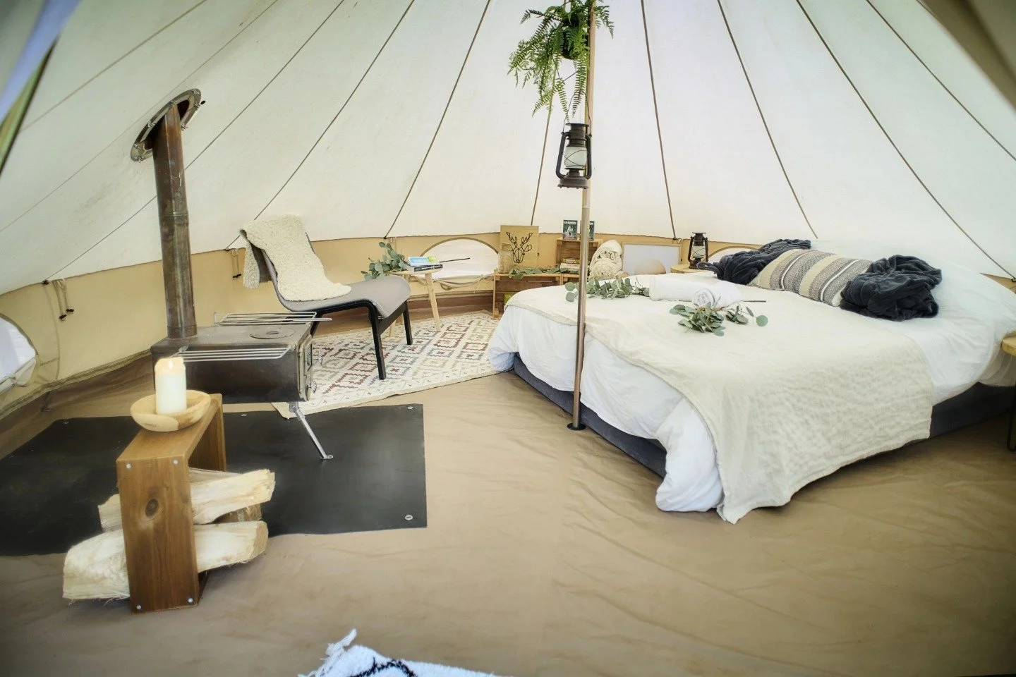 Intérieur d'une tente avec lit, lampe, fauteuil, tapis, cheminée et décoration naturelle.