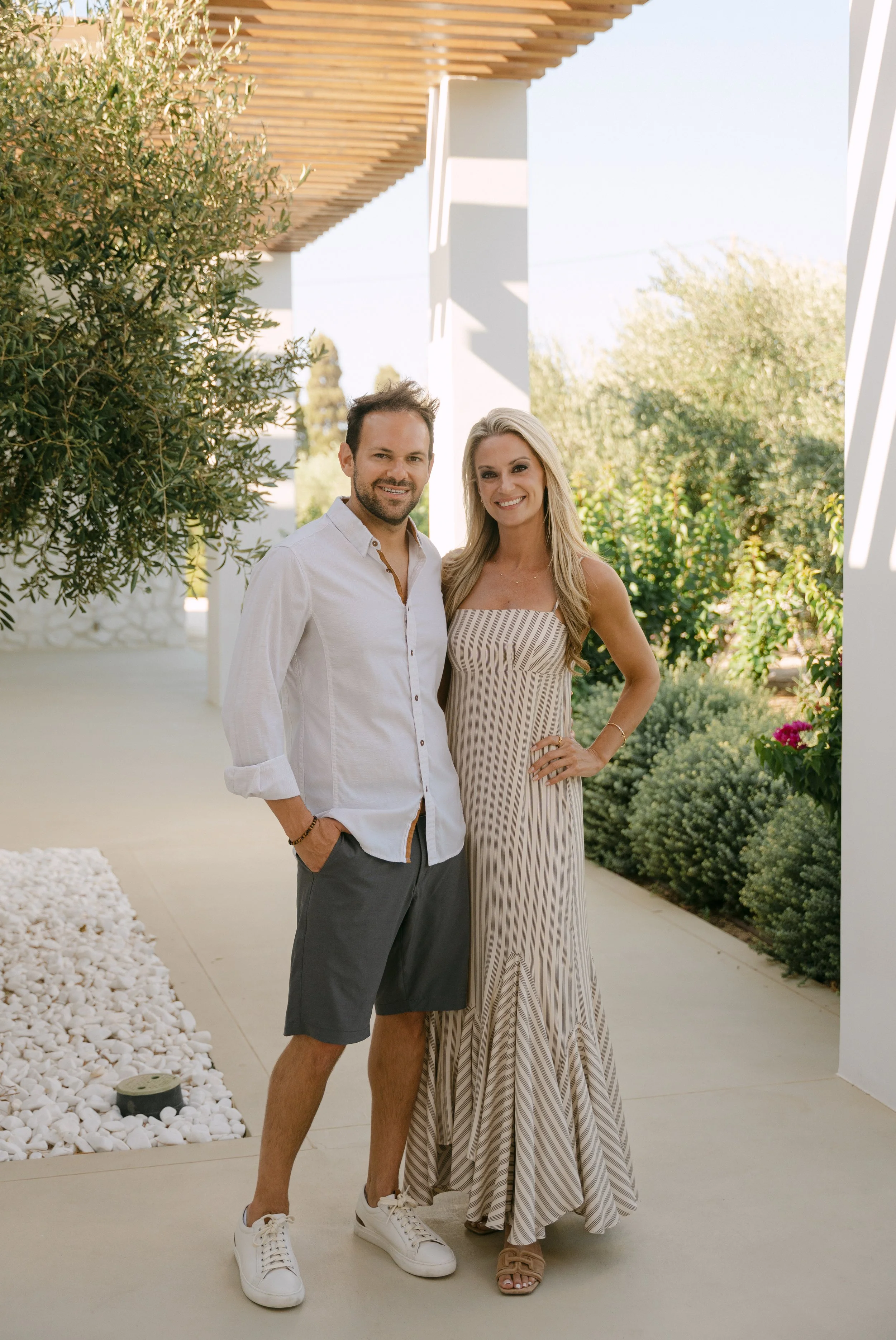 A man and woman standing outdoors on a patio with greenery, smiling at the camera.