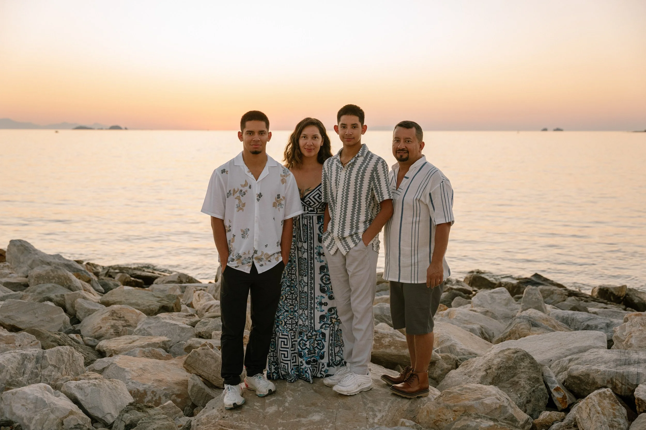 A family of four standing on rocks by the water during sunset.