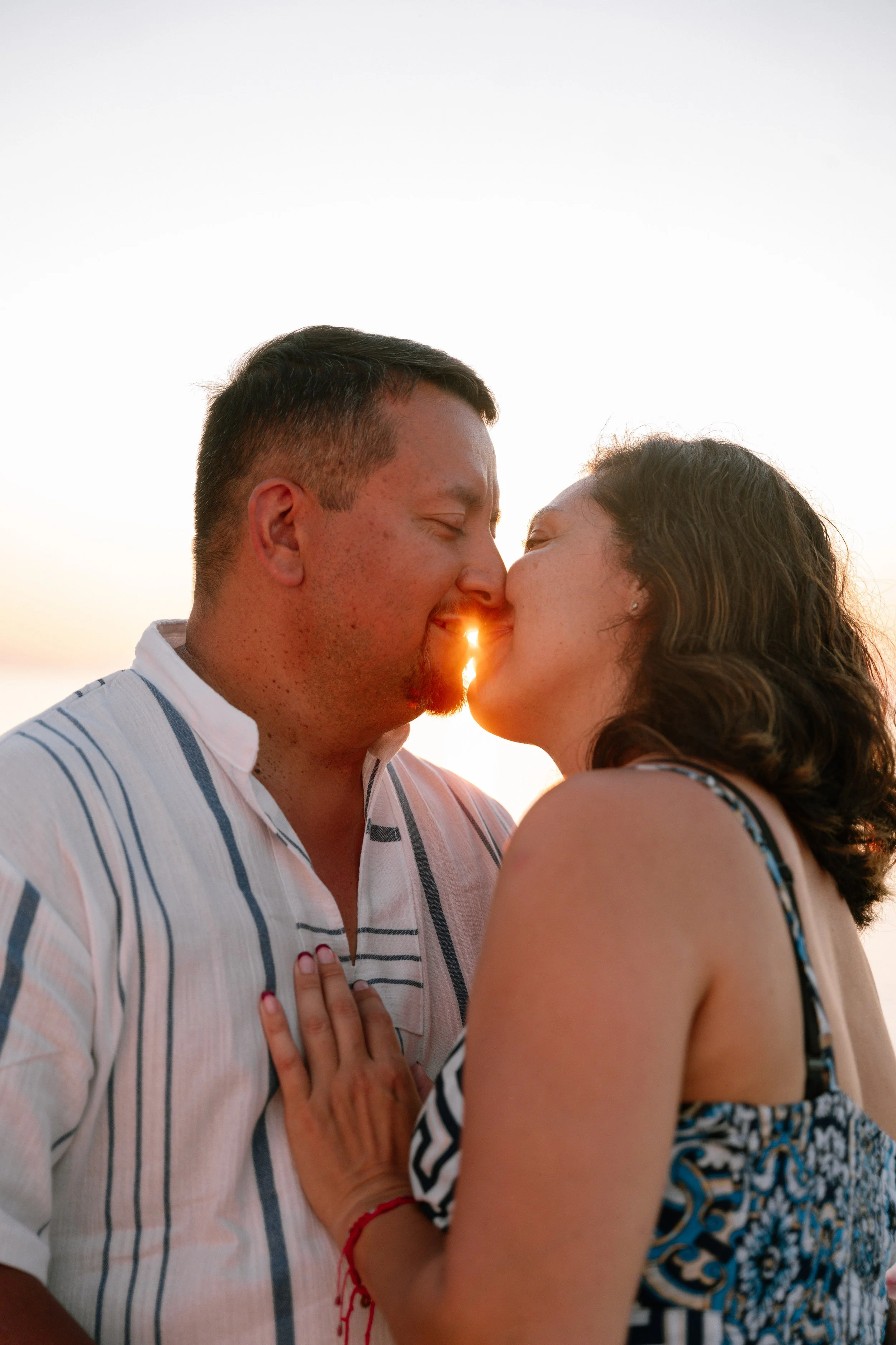 A couple kissing during sunset, with the sun peeking through their noses.