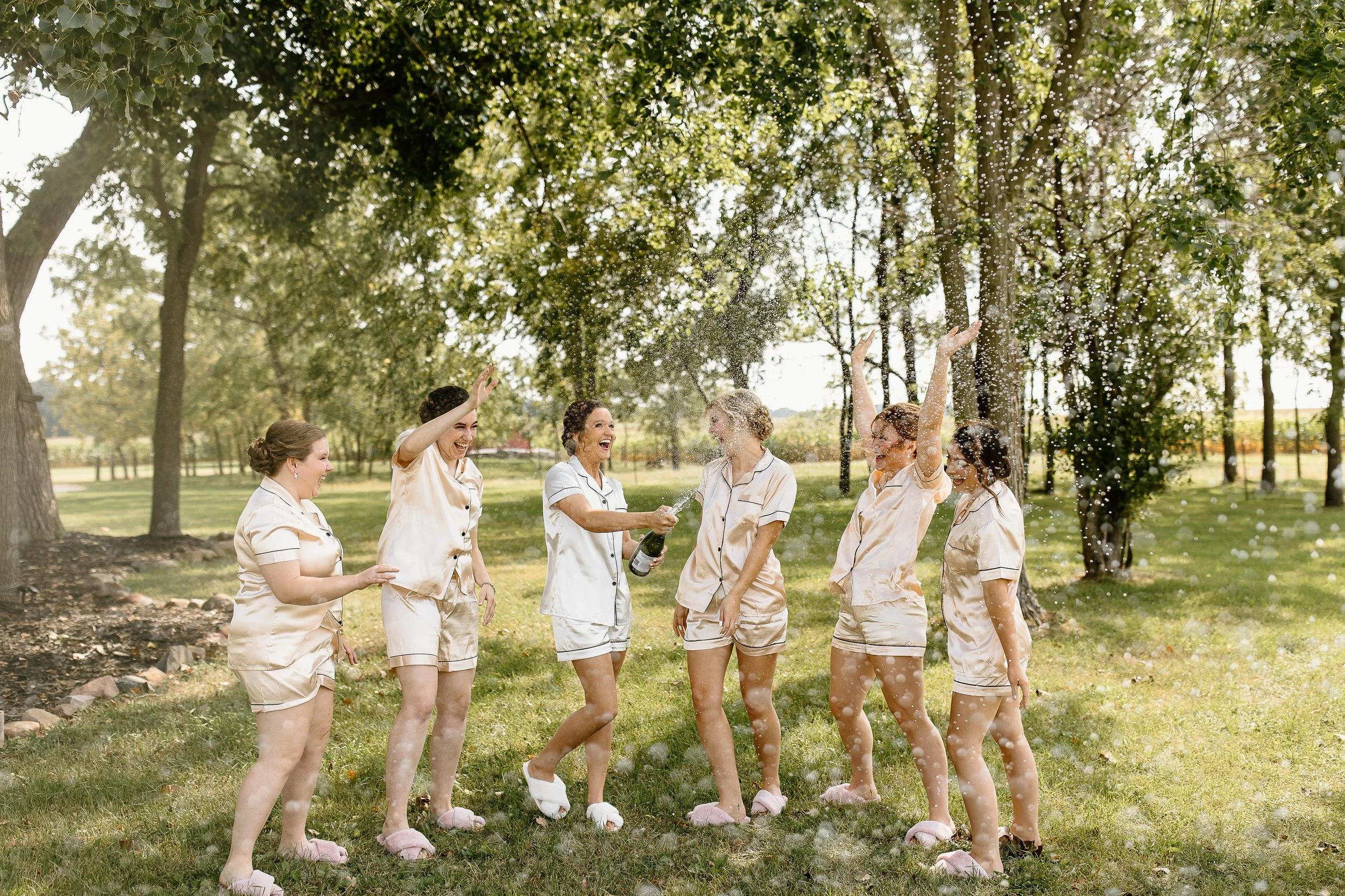 Group of women in pajamas celebrating and spraying champagne at a Wisconsin barn wedding venue