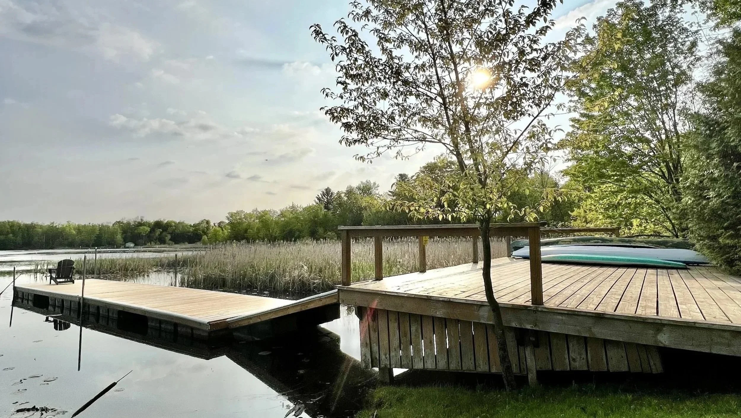 Wooden dock at Marmora Retreats, overlooking a peaceful lake surrounded by trees and reeds on a clear day