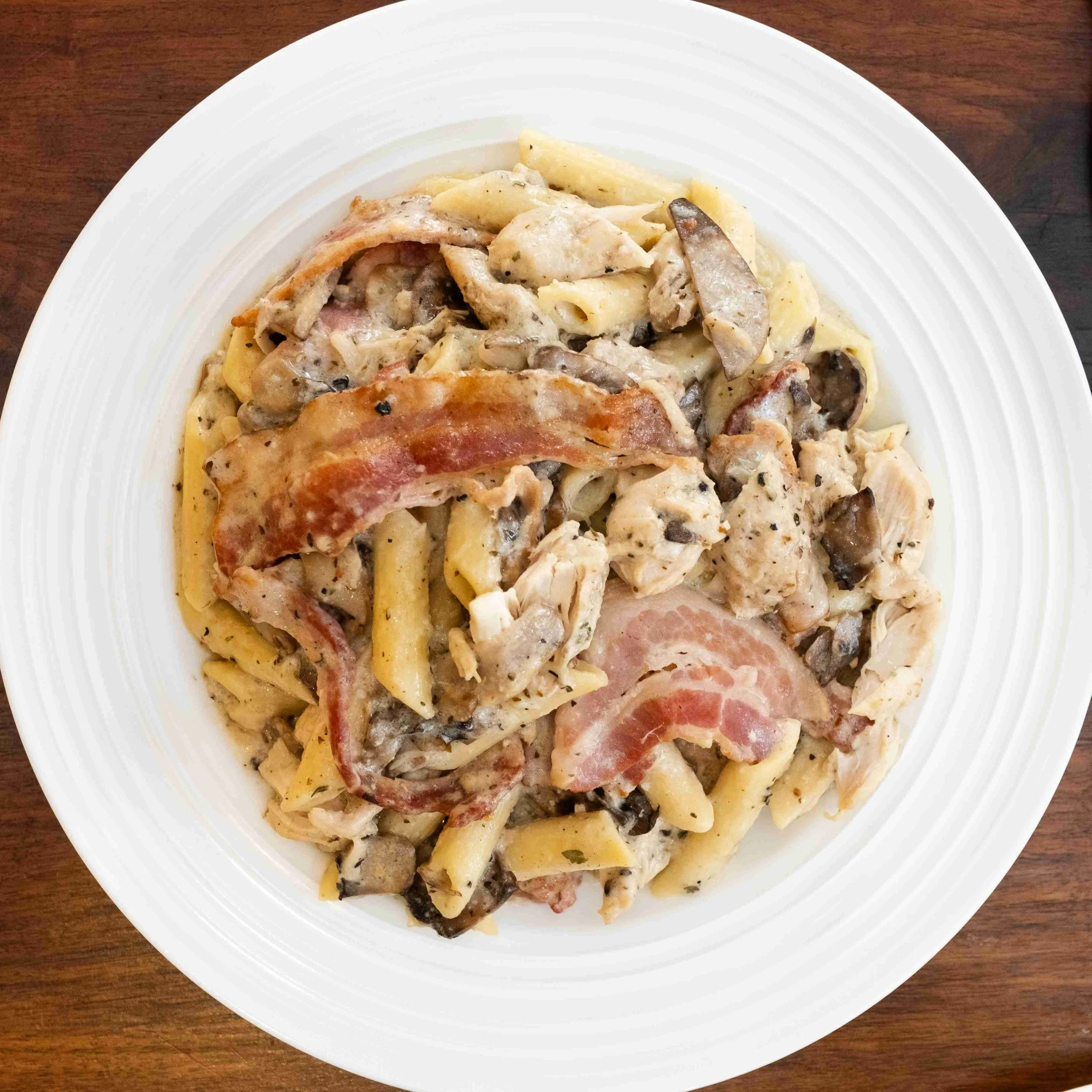 Plate of creamy pasta with mushrooms, bacon, chicken, and herbs on a white dish.