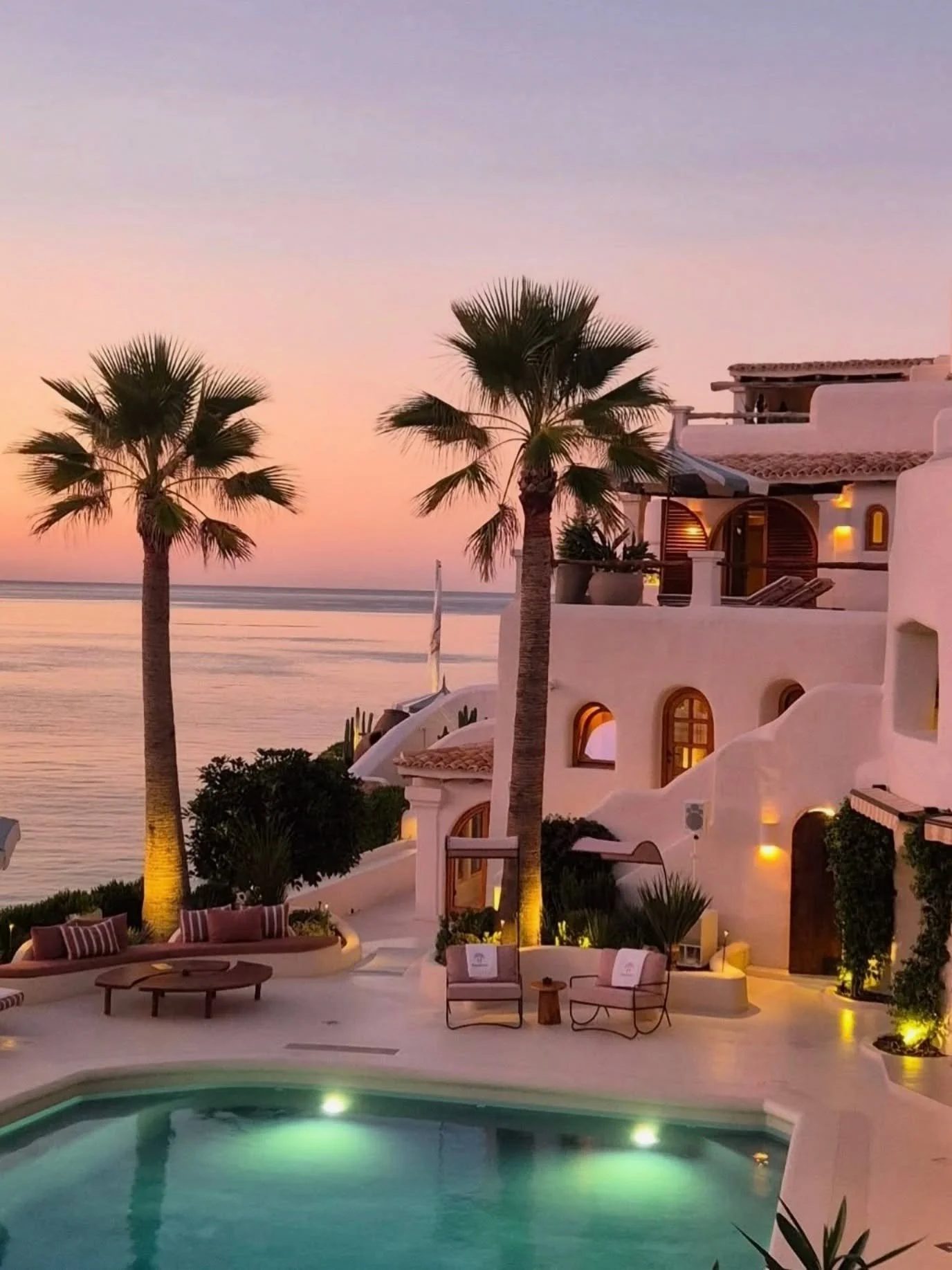 As dusk settles over Cala Xarraca, the villa begins to glow. 
Whitewashed curves catch the last blush of the day, while the palms stand sentinel against a sea of lavender and gold. 
Soulful living embodied. 
Photography @travelhealingcomforts 
#i