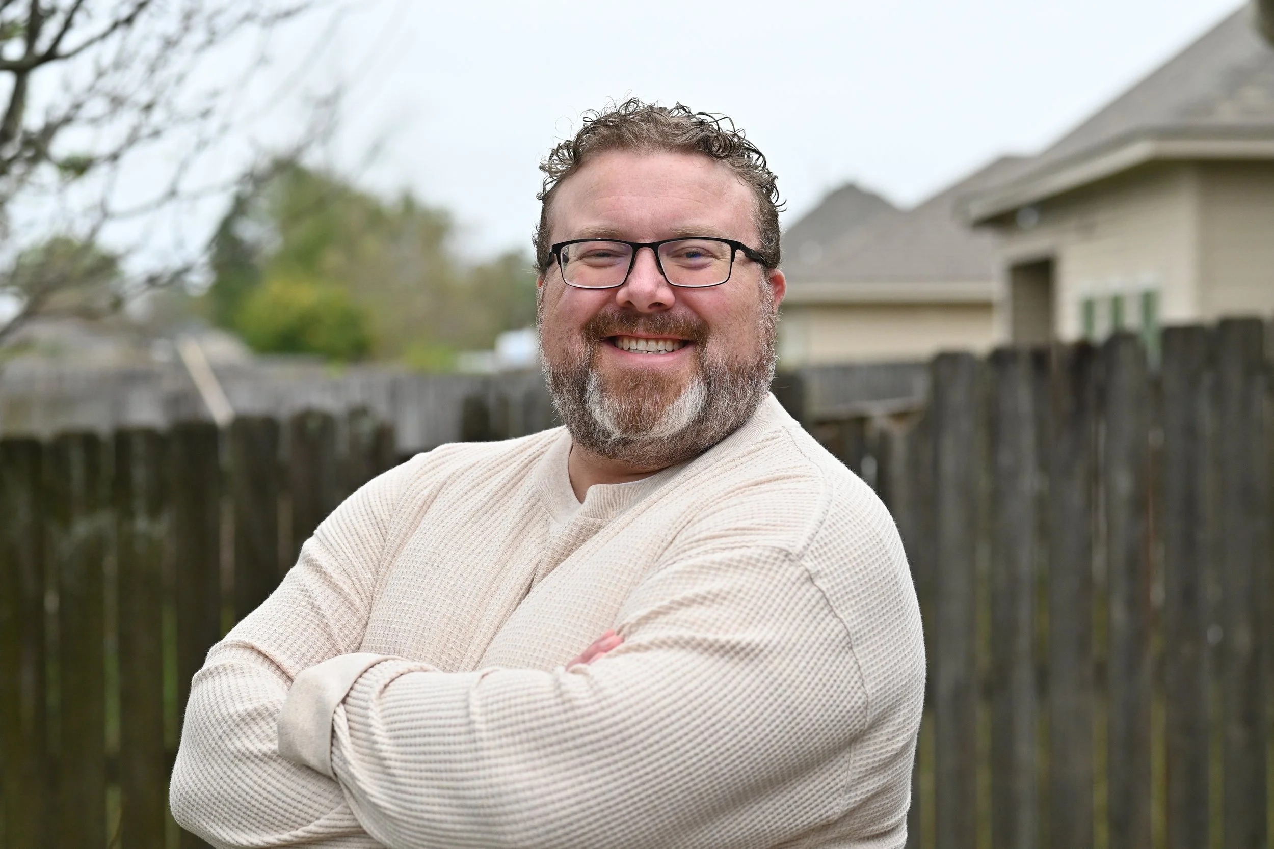 Business book ghostwriter Derek Lewis smiling in a cream pullover and glasses, standing outdoors in a casual backyard setting