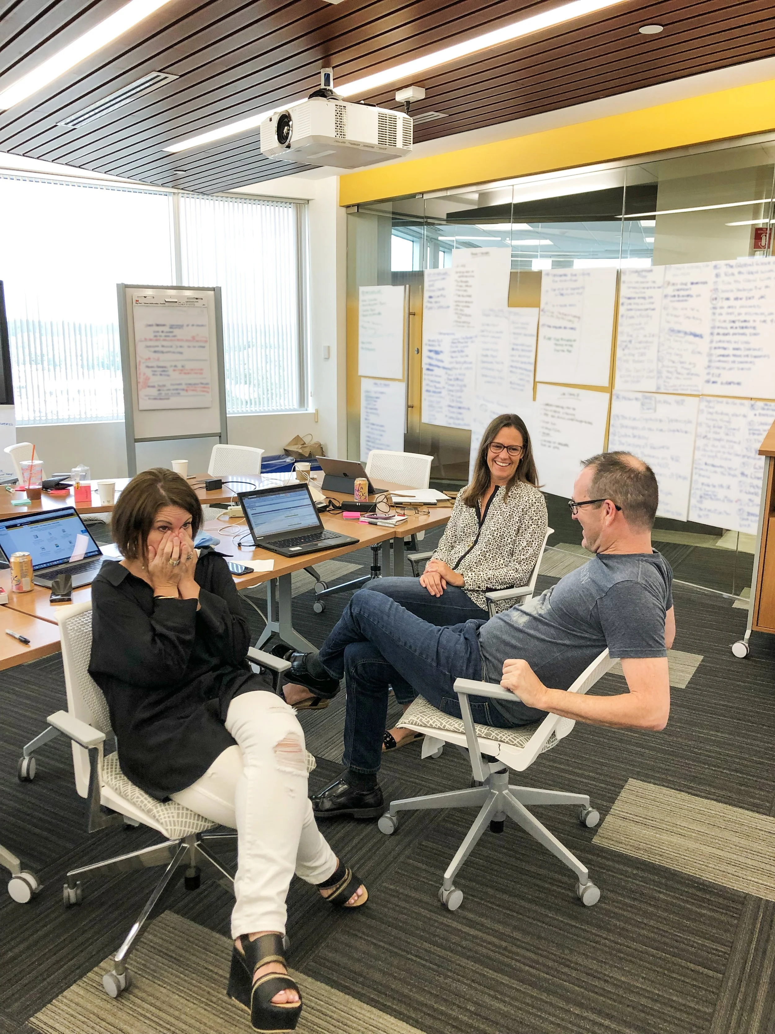 Three business book authors laughing during a creative brainstorming session with sticky notes on the wall, illustrating the enjoyable ghostwriting discovery process.