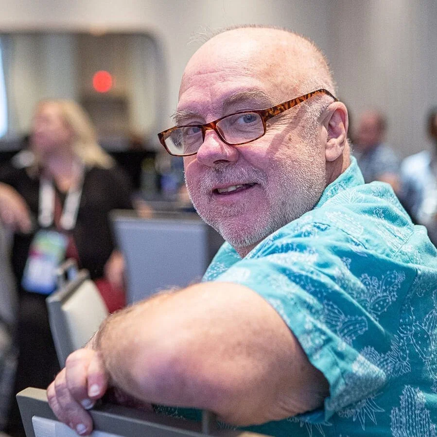 Business book ghostwriting client John Willis smiling in a blue shirt at a conference, author of The DevOps Handbook and Deming's Journey to Profound Knowledge