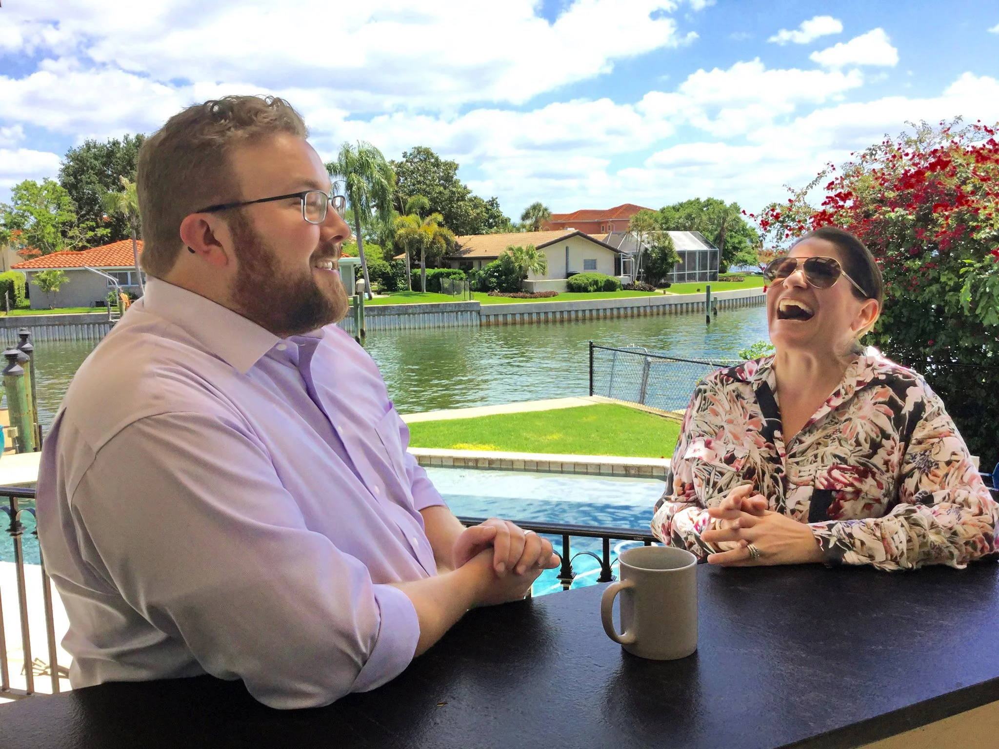 Business book ghostwriter Derek Lewis (left) in a pink shirt and a client laughing together overlooking a Florida canal, demonstrating the close personal rapport built with authors