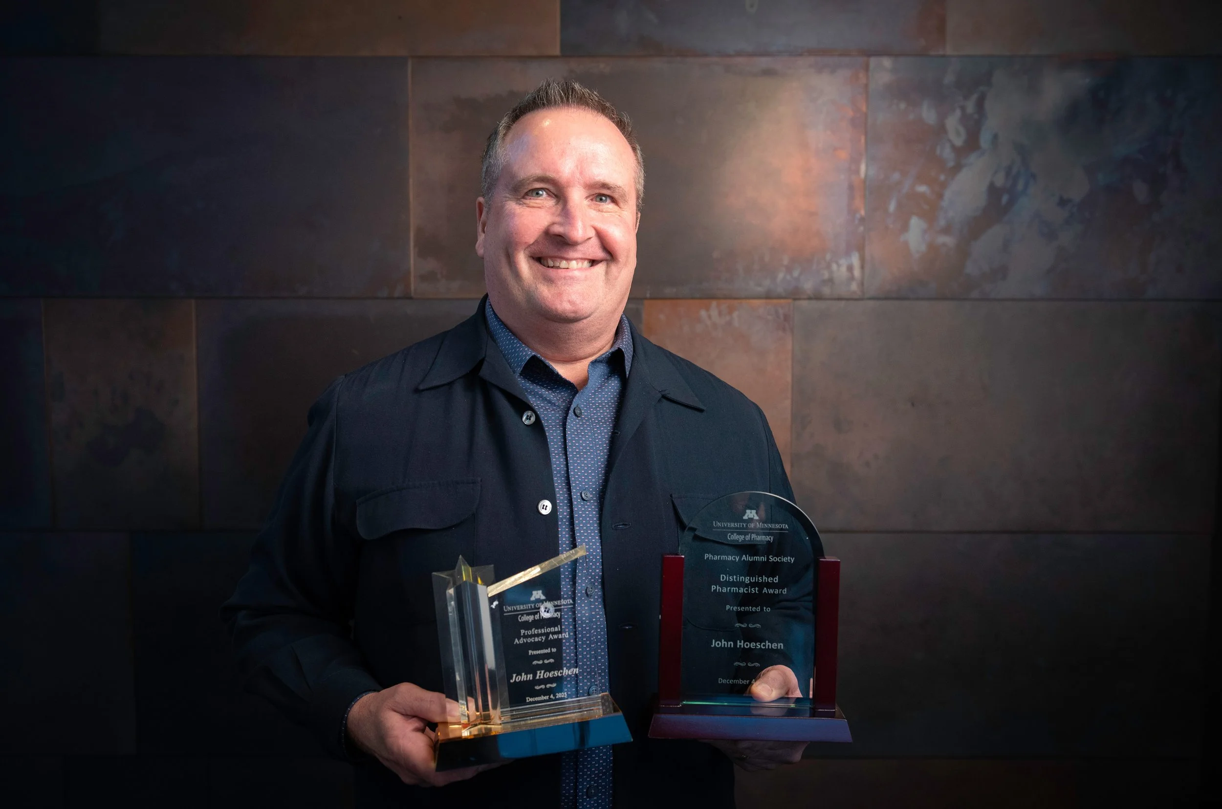 John Hoeschen stands with his 2025 Distinguished Pharmacist and Professional Advocacy Awards from the University of Minnesota College of Pharmacy & Pharmacy Alumni Society
