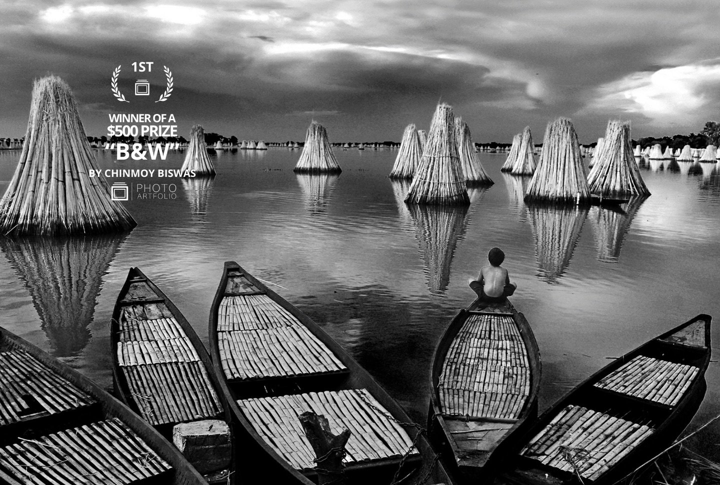 📷 B&amp;W: The Poetry of Light &amp; Shadow
1st Place
&ldquo;Lonely&rdquo; by Chinmoy Biswas @careofbiswas 

Stillness stretches across the frame.
Boats rest. Water listens.
A single figure sits at the edge of silence.
In &ldquo;Lonely,&rdquo; light
