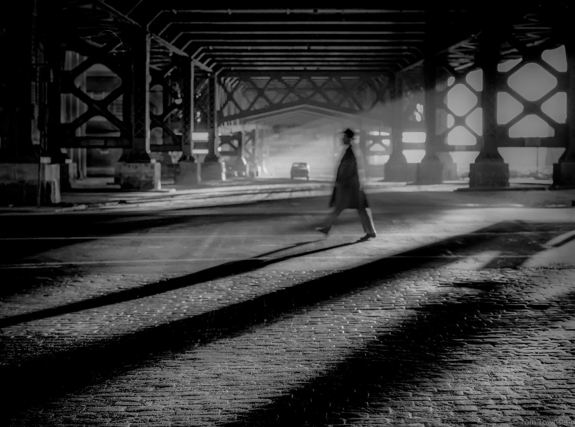 📷 B&amp;W: The Poetry of Light &amp; Shadow
&ldquo;Walking into Destiny&rdquo; by Tom Townsend 

A lone figure cuts through light and shadow &mdash; motion softened into atmosphere. The industrial geometry stands rigid while the human presence drift