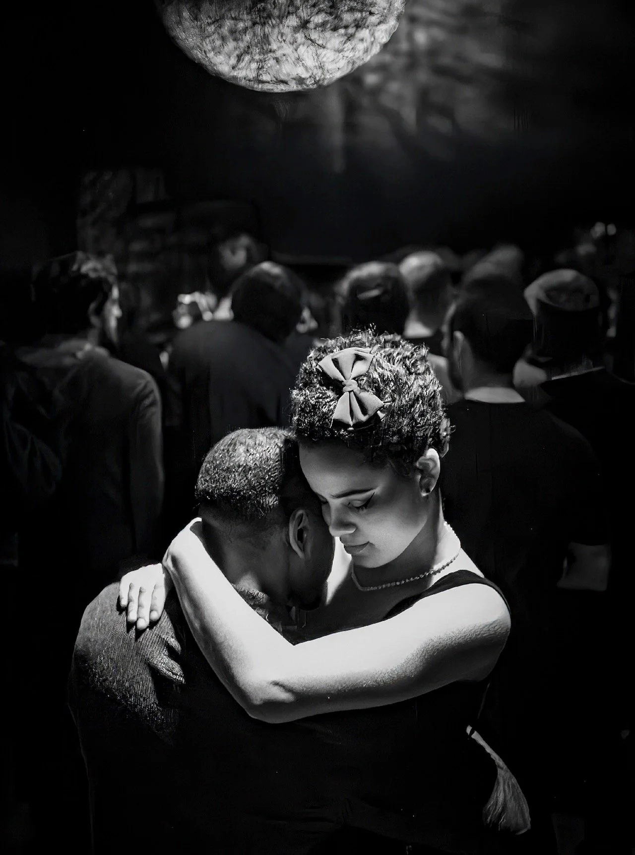 📷 B&amp;W: The Poetry of Light &amp; Shadow
&ldquo;In the Quiet of Each Other&rdquo; by Reza Assar

In the middle of a crowded room, a couple disappears into a quiet embrace. A single beam of light isolates them from the surrounding figures, turning