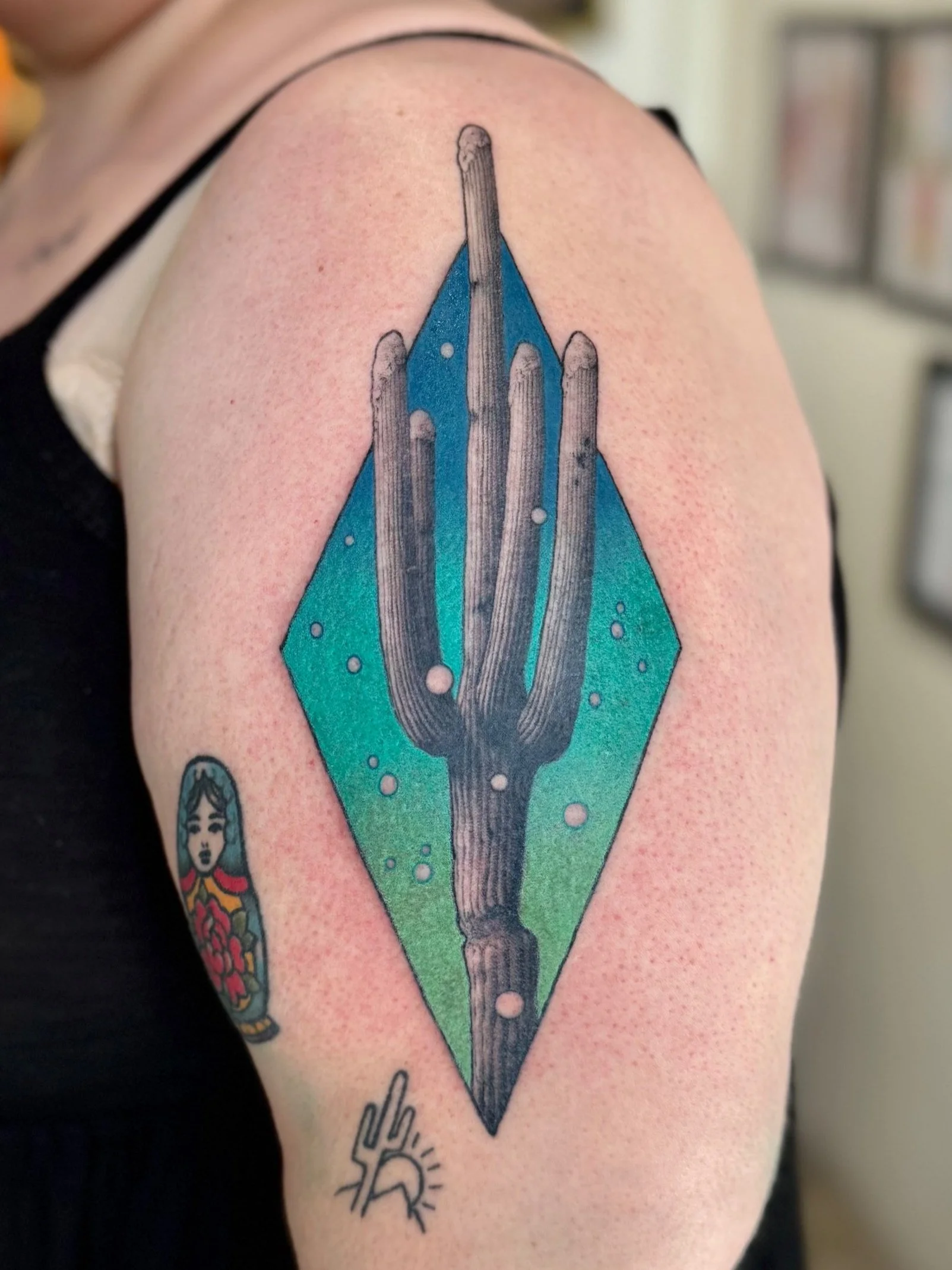 Tattoo of a stylized spear or arrow with a blue background and circles, and a small person figurine tattoo below on the arm.