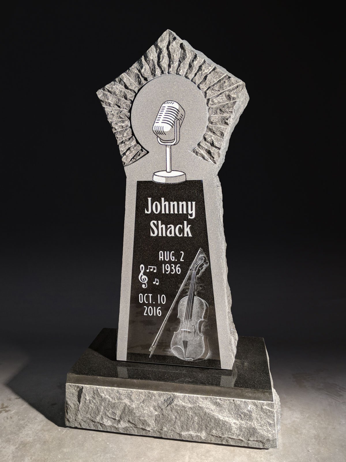 Memorial plaque with a microphone and musical notes, dedicated to Johnny Shack, with dates August 2, 1936 to October 10, 2016, featuring a violin and bow engraving.