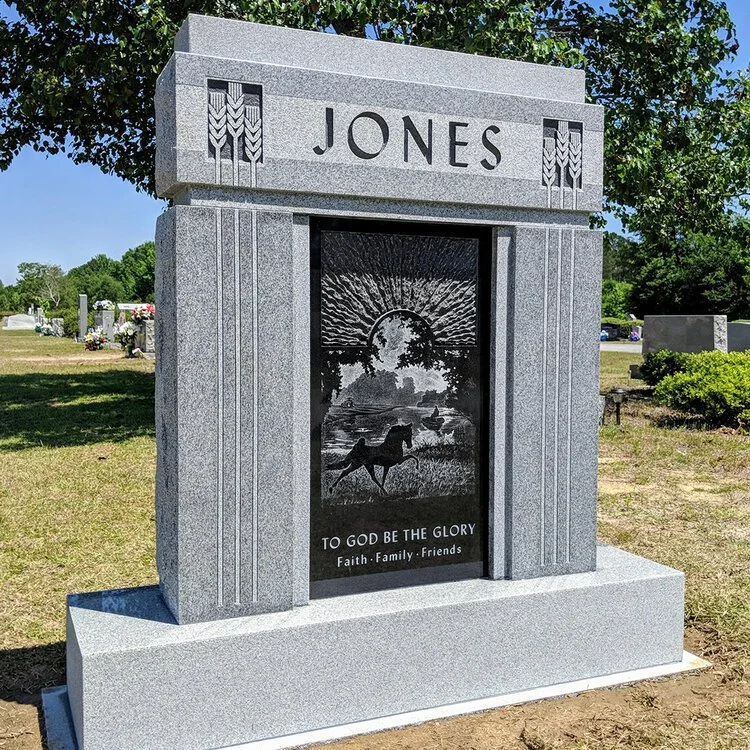 Gravestone with the name 'Jones' and religious inscription 'To God Be The Glory' at a cemetery, featuring a silhouette of a horse and landscape scene engraved on it.