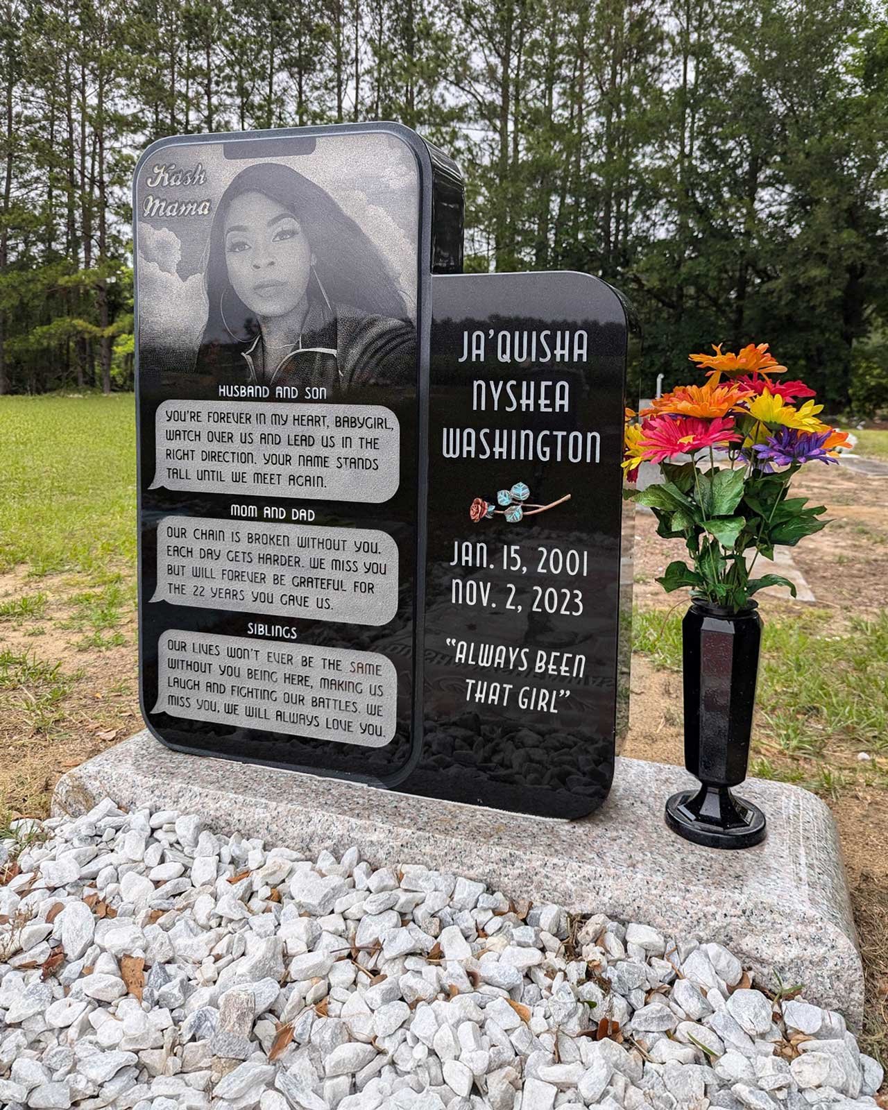 A black gravestone with a picture of a woman wearing a hat, and flowers next to it. The gravestone has personal messages for Ja'quisha Nyshea Washington, born January 15, 2001, and died November 2, 2023. It includes her photo, name, birth and death d