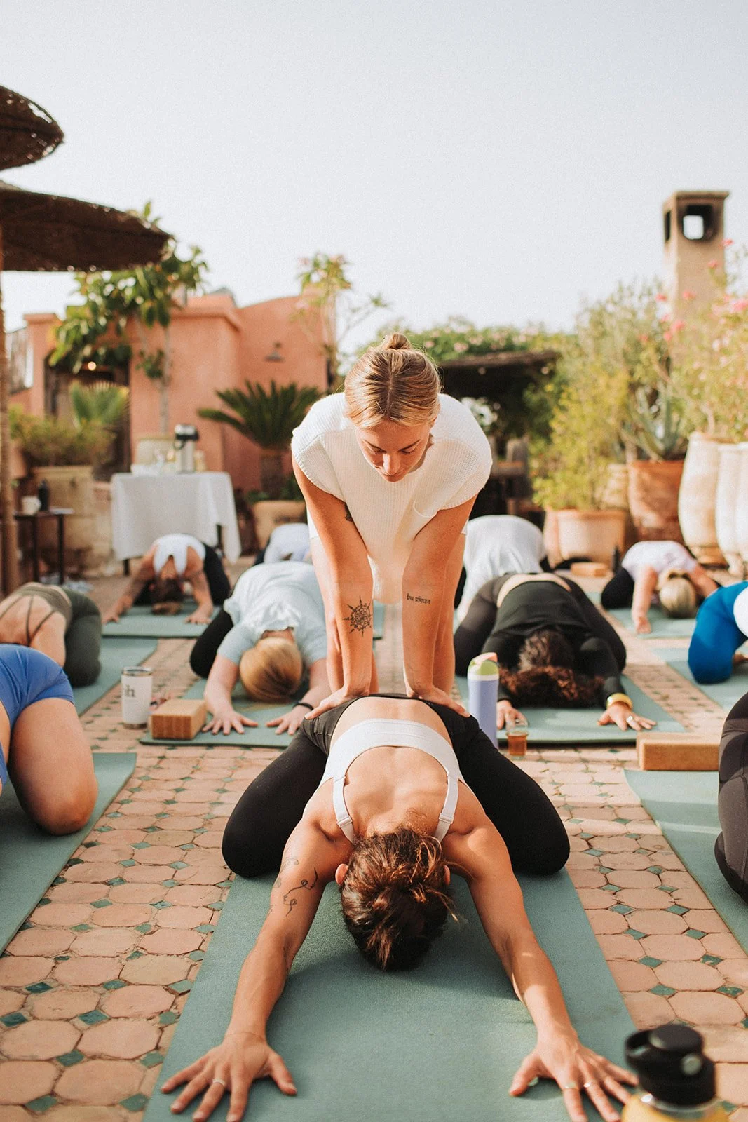 Yoga teacher assisting student during outdoor retreat yoga class on a patio at Flow State Wellness.