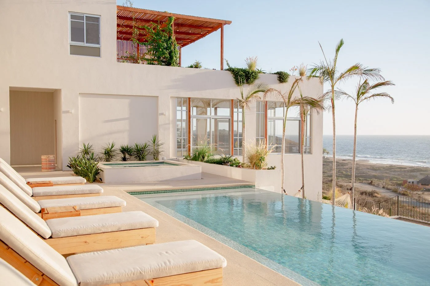 Luxury modern house with an infinity pool overlooking the ocean, with palm trees and lounge chairs.