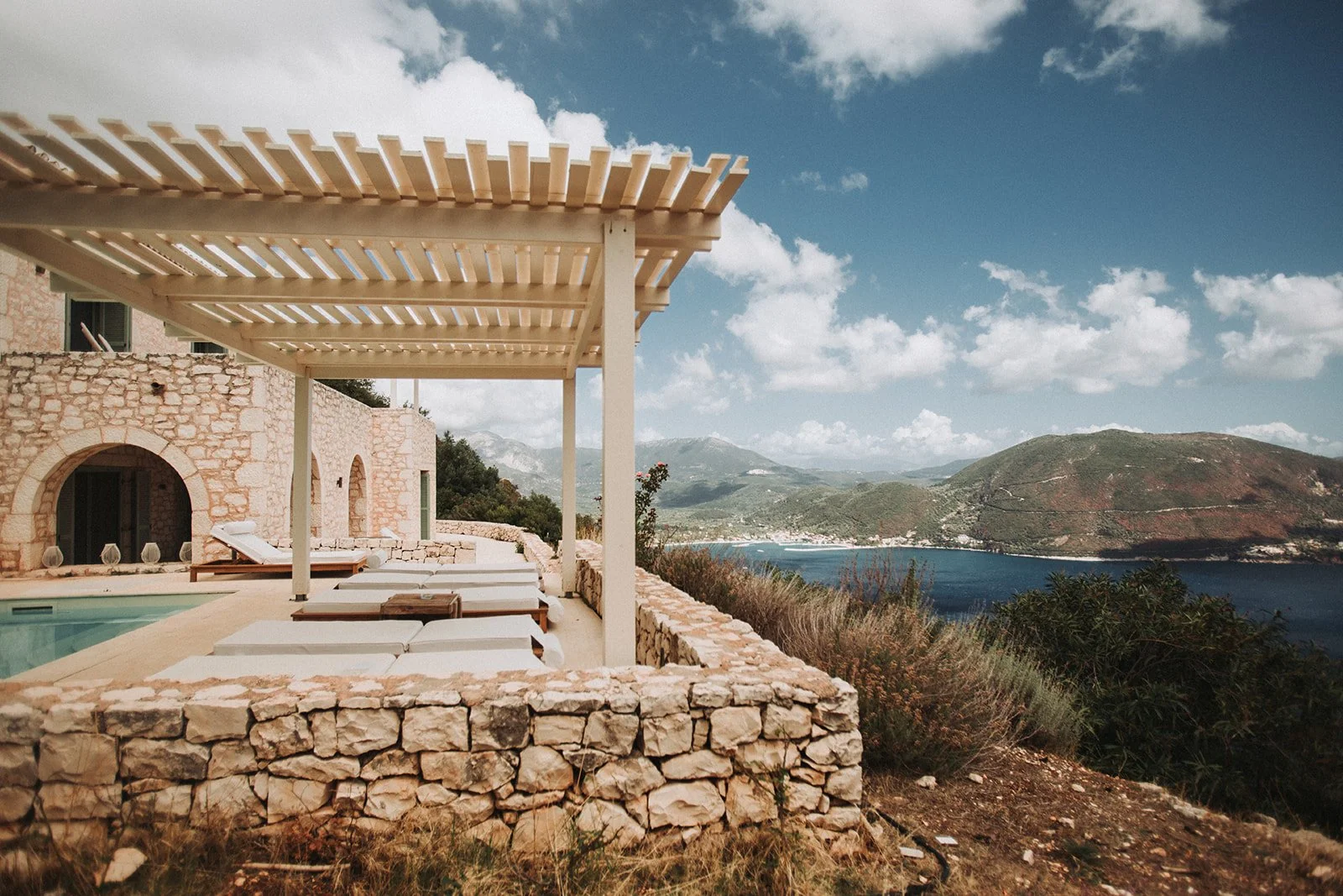 Luxury retreat villa with pool and lounge chairs overlooking a coastal bay and mountains, ideal for yoga and wellness retreats.